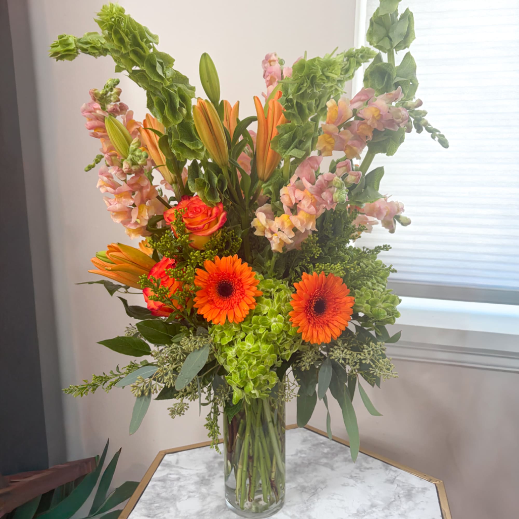 Tall mixed bouquet with orange lilies, gerbera daisies, roses, and pink snapdragons in a glass vase