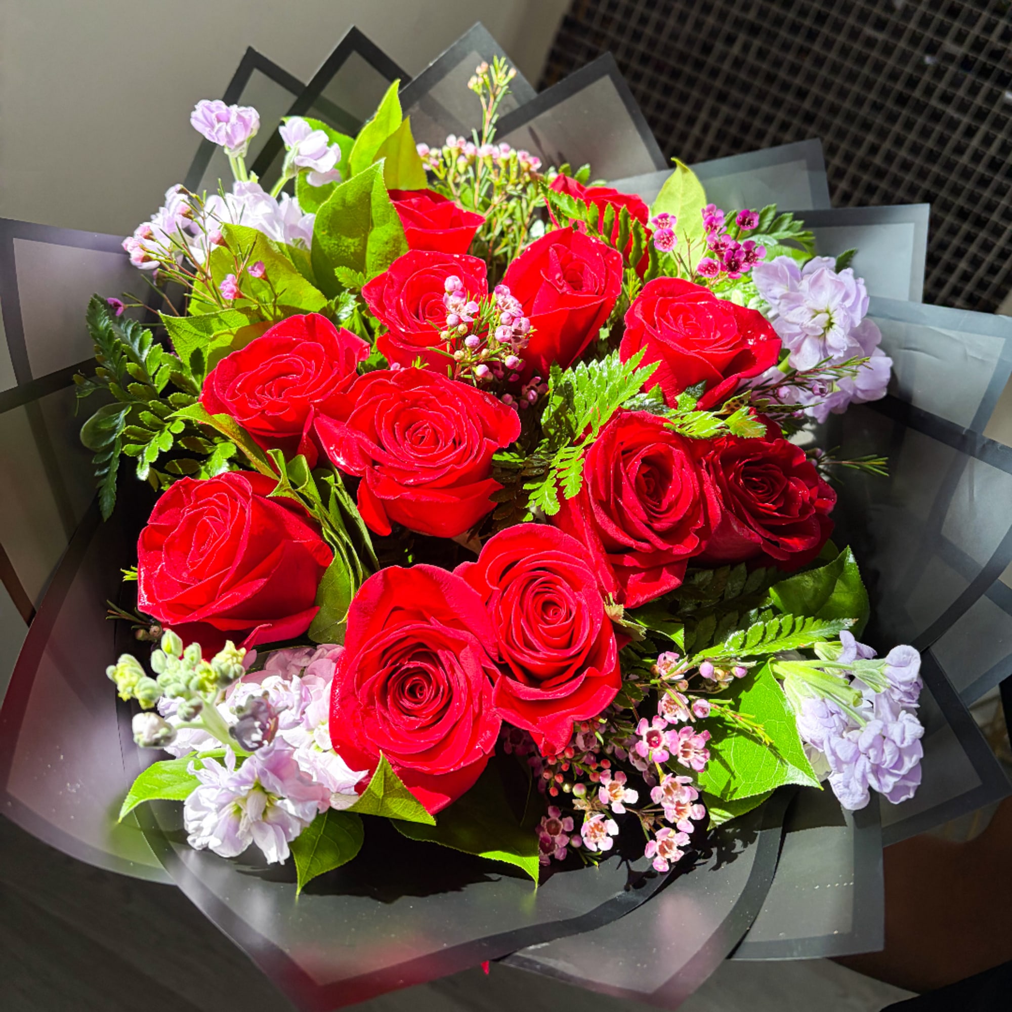 Bouquet of red roses with pale lavender filler flowers wrapped in black paper