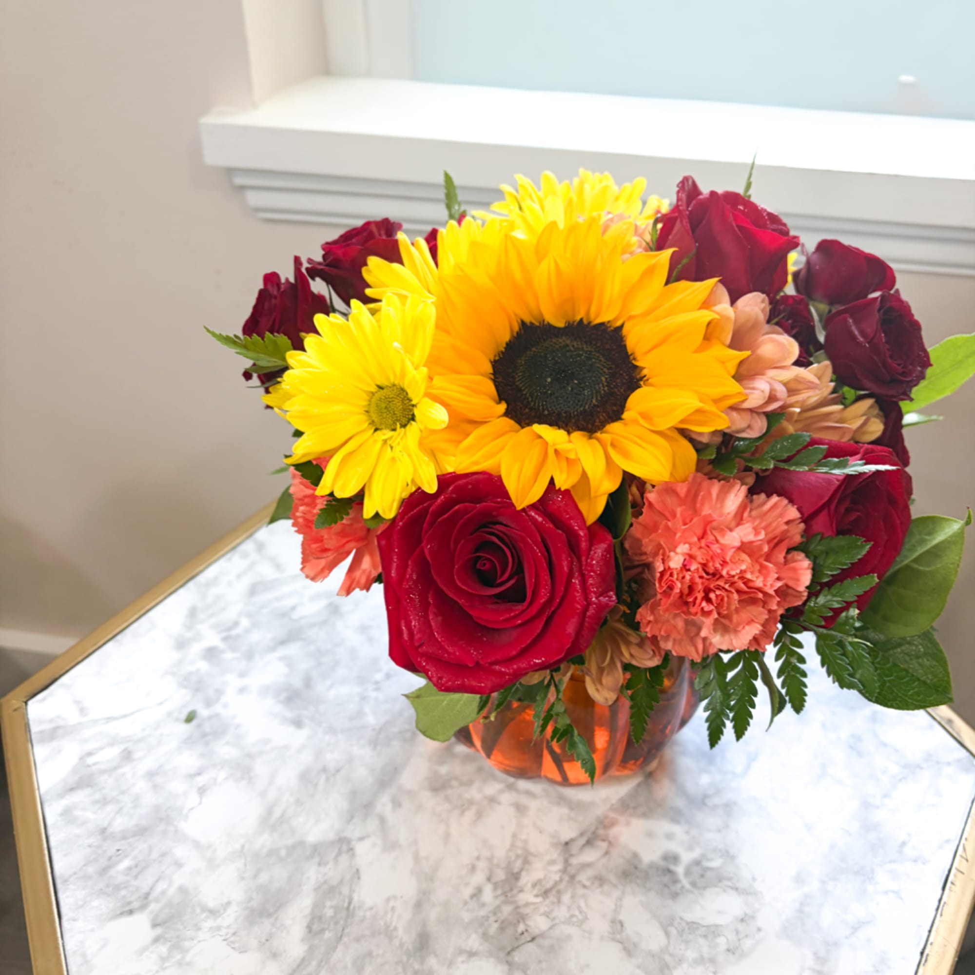 Bouquet of sunflowers, red roses, and peach carnations in a glass vase