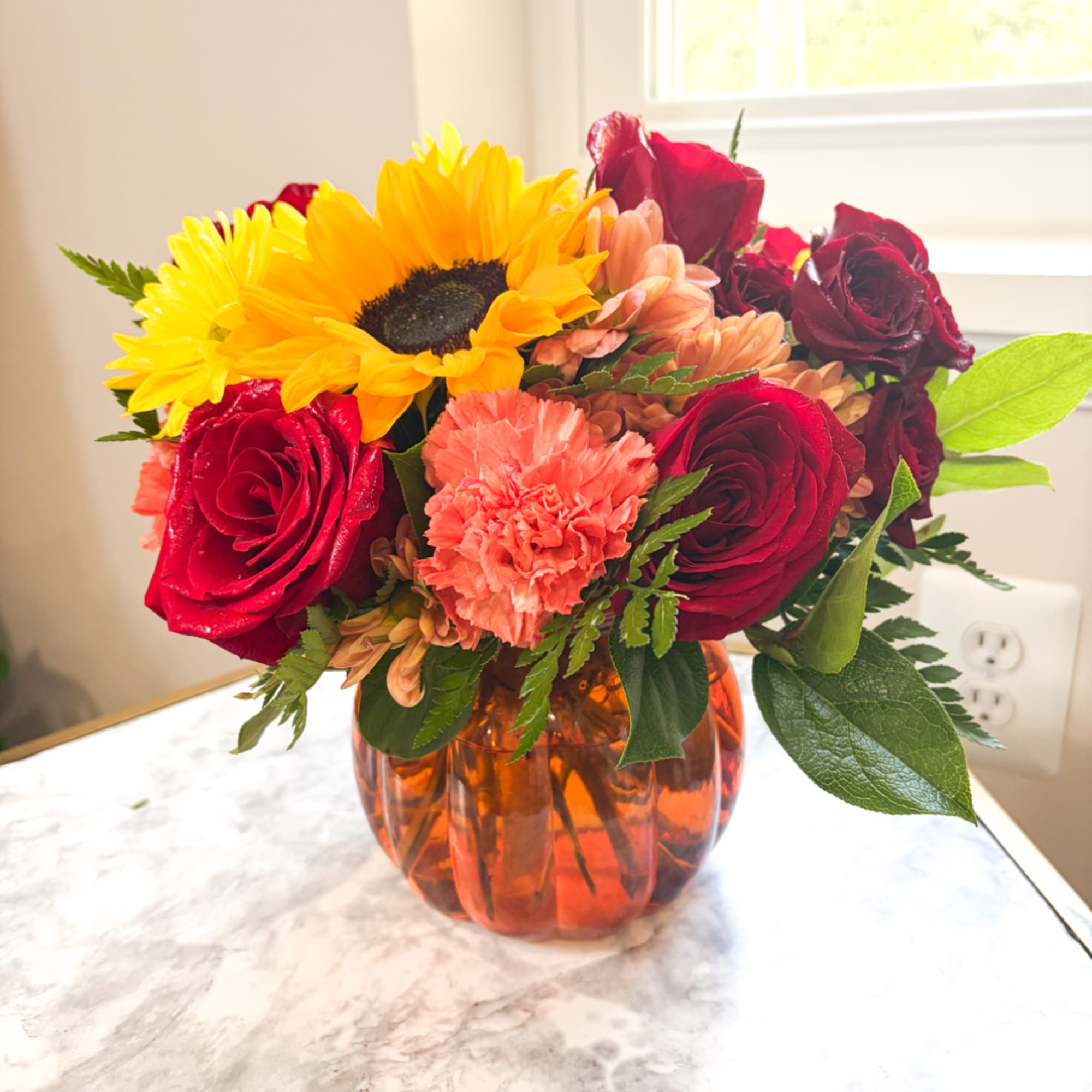 Bouquet of sunflowers, red roses, and peach carnations in an amber vase