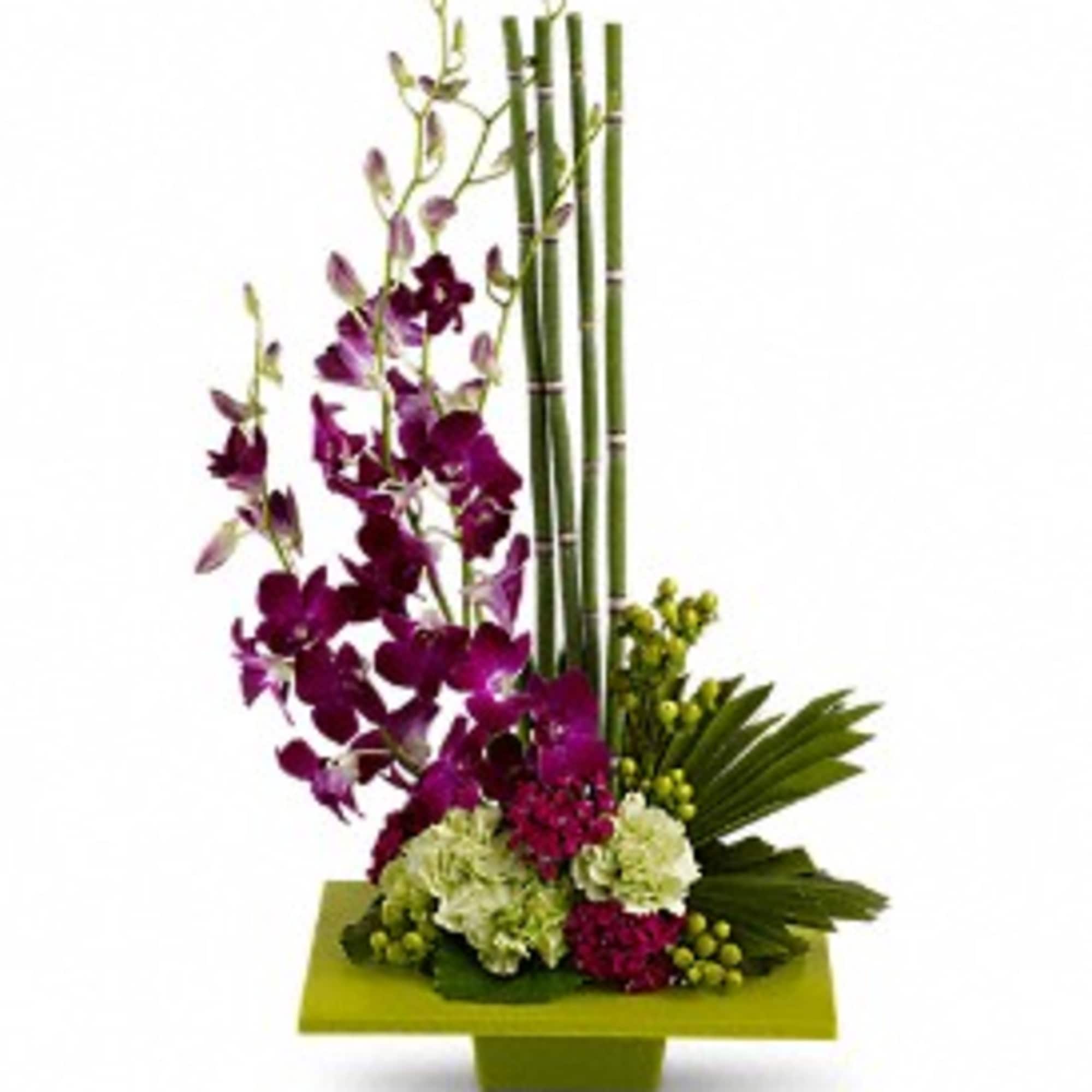 Modern arrangement of purple orchids and green and pink flowers with tall bamboo in a low green rectangular container