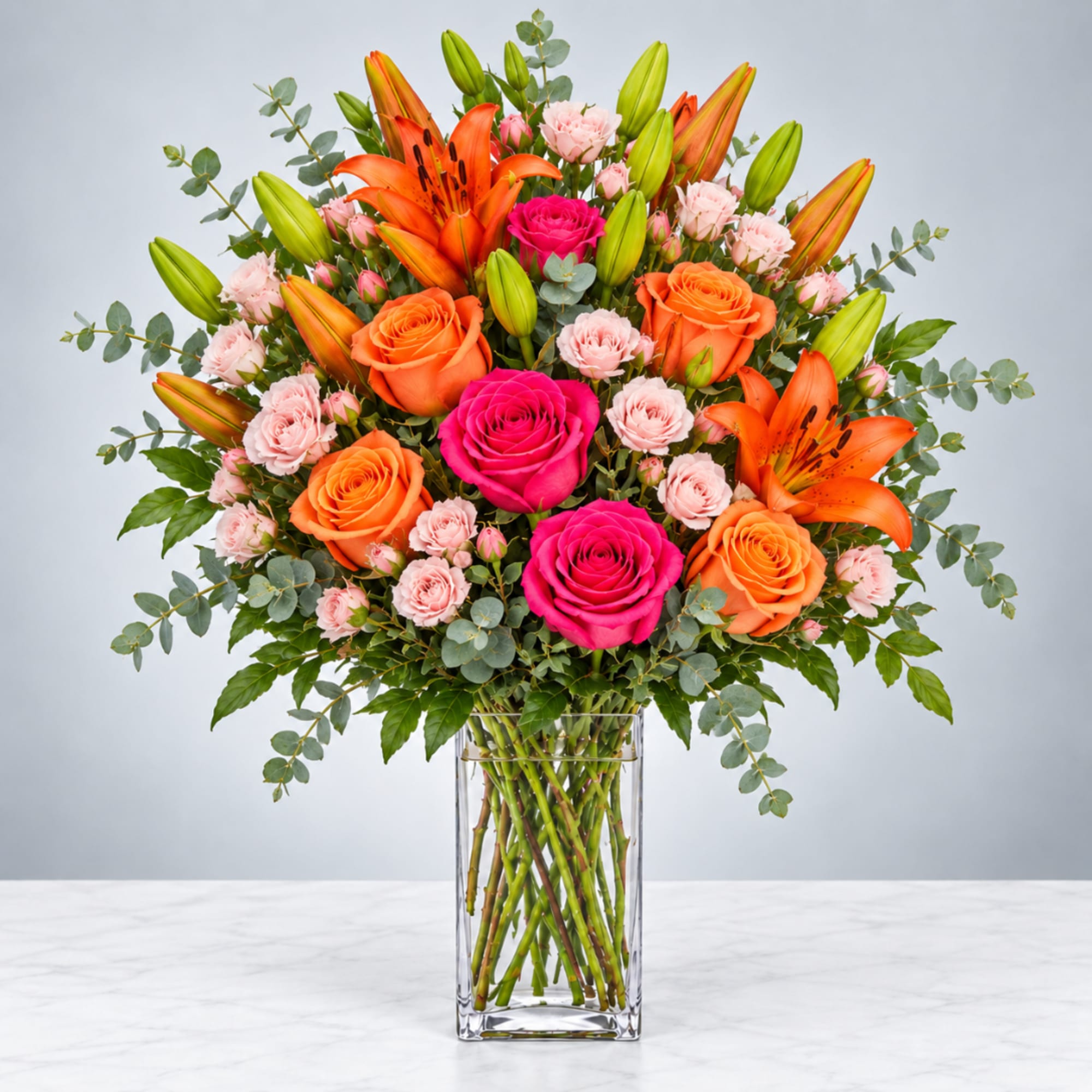 Bright mixed bouquet of roses, lilies, and carnations in a clear glass vase