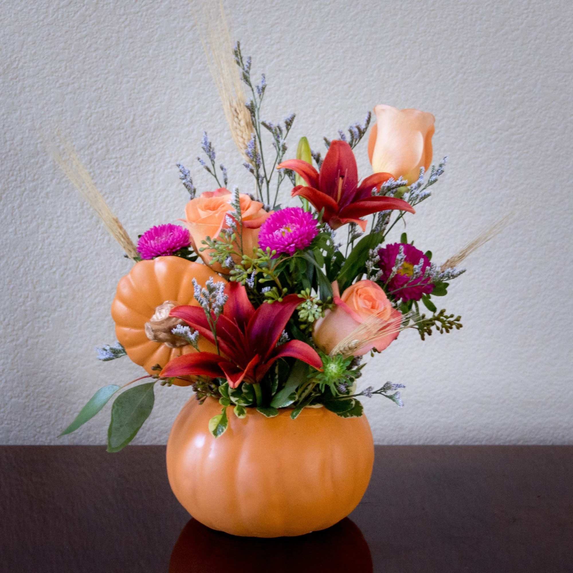 Pumpkin-shaped vase with orange roses, red lilies, and pink flowers