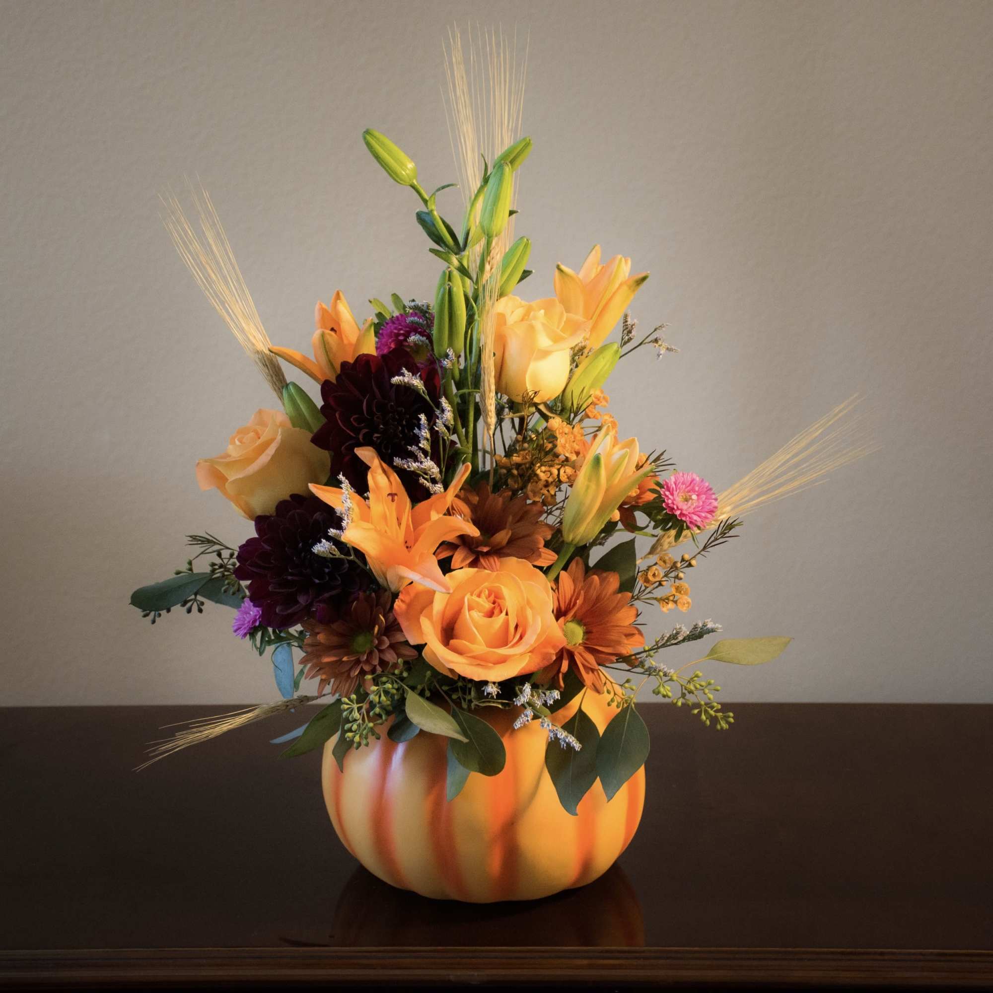 Autumn floral arrangement in a pumpkin-shaped container with orange and purple blooms