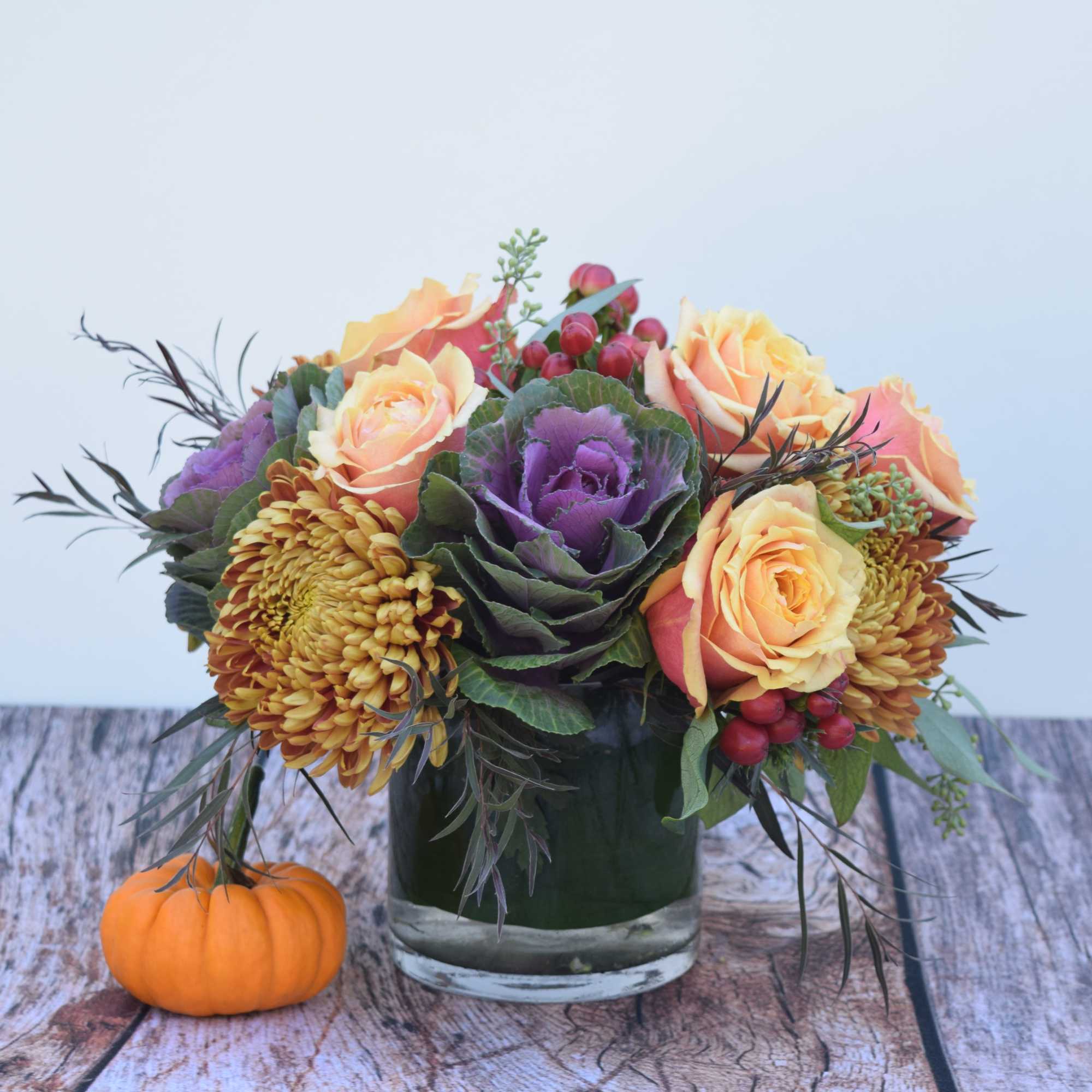 Mixed bouquet in a glass vase with a small pumpkin beside it