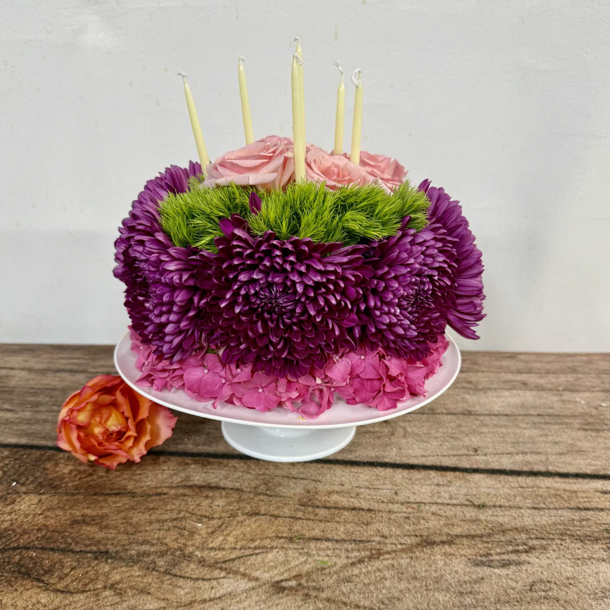 Pink and purple floral cake with candles on a white stand