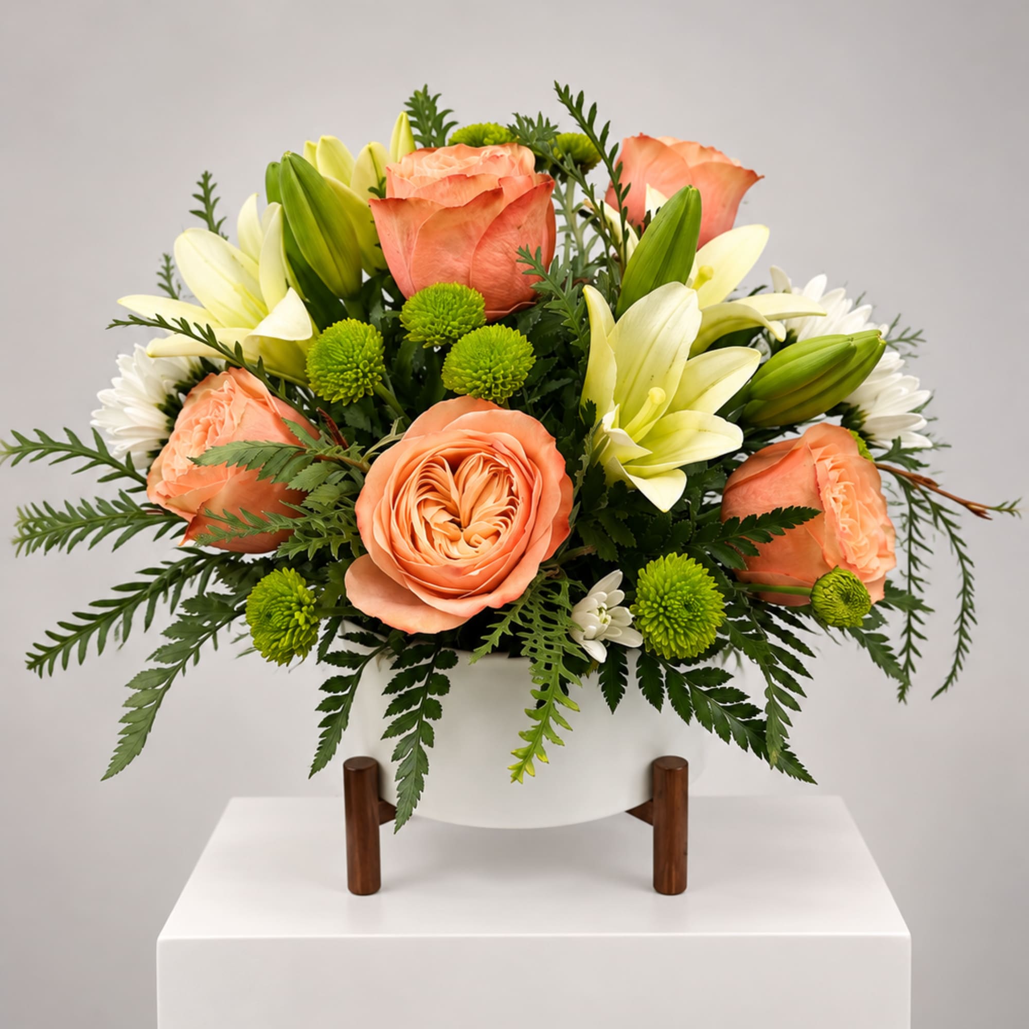 Peach roses and white lilies arranged in a white vase