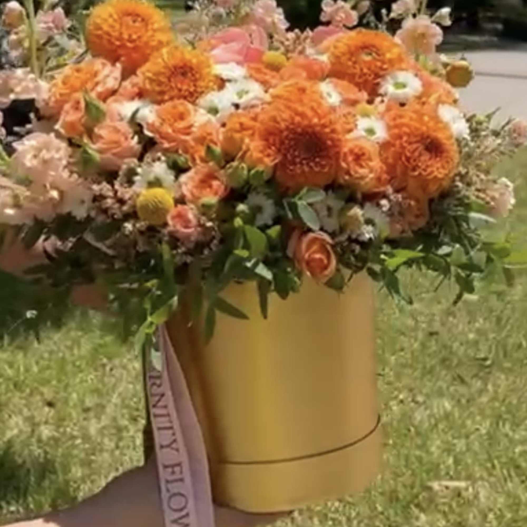 Orange and peach floral arrangement in a gold box with a ribbon
