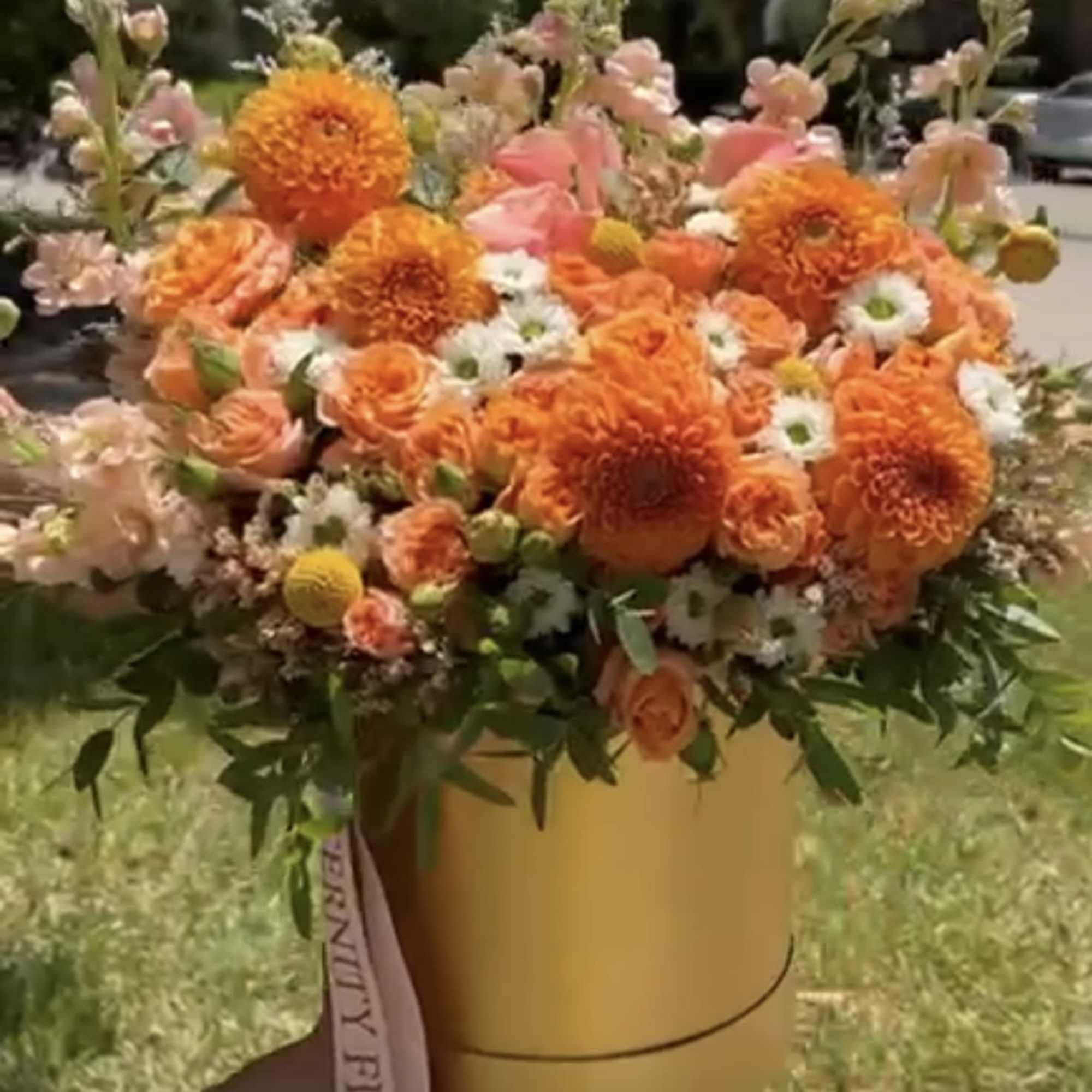 Orange and peach flower arrangement in a round hat box