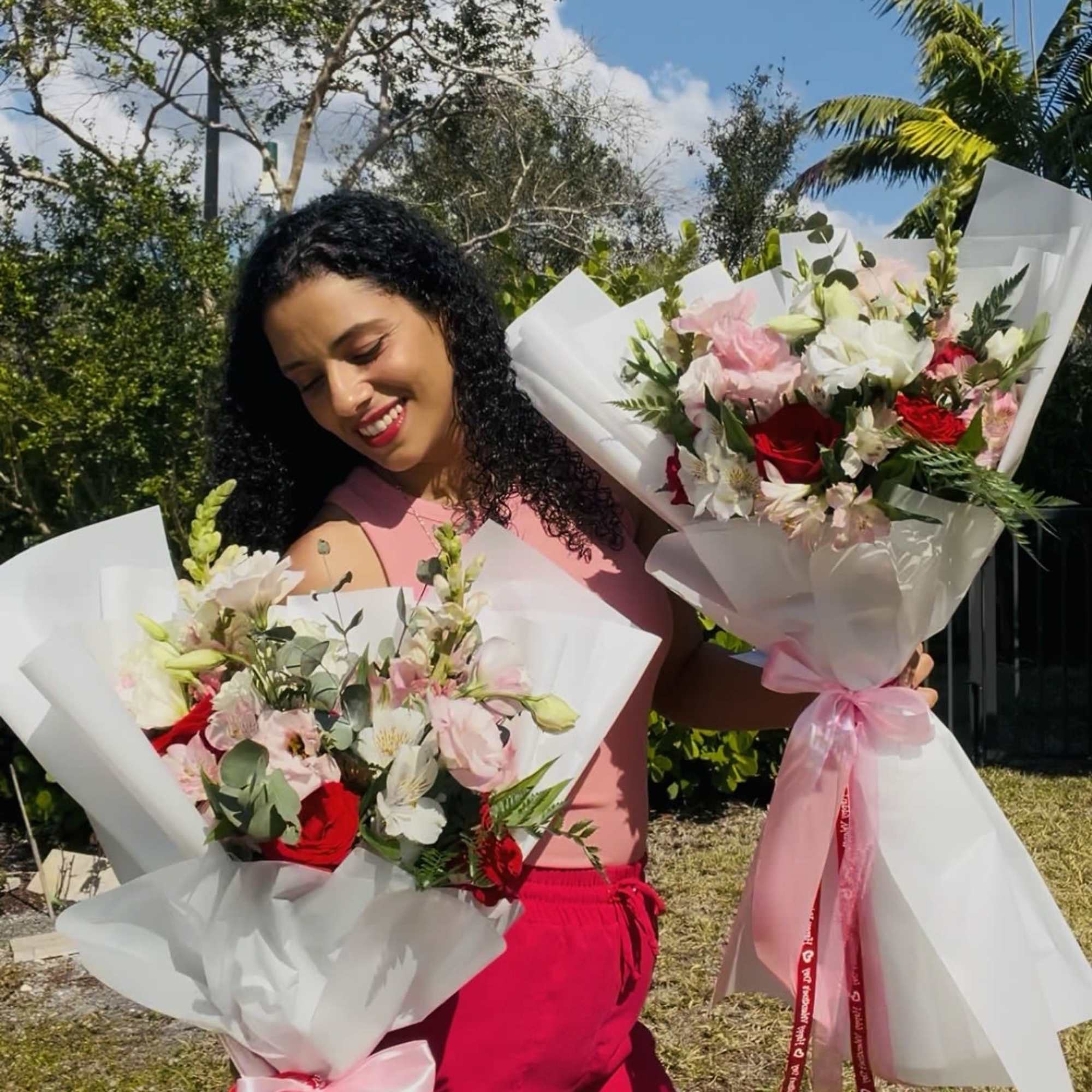 Woman holding two wrapped bouquets of pink, red, and white flowers