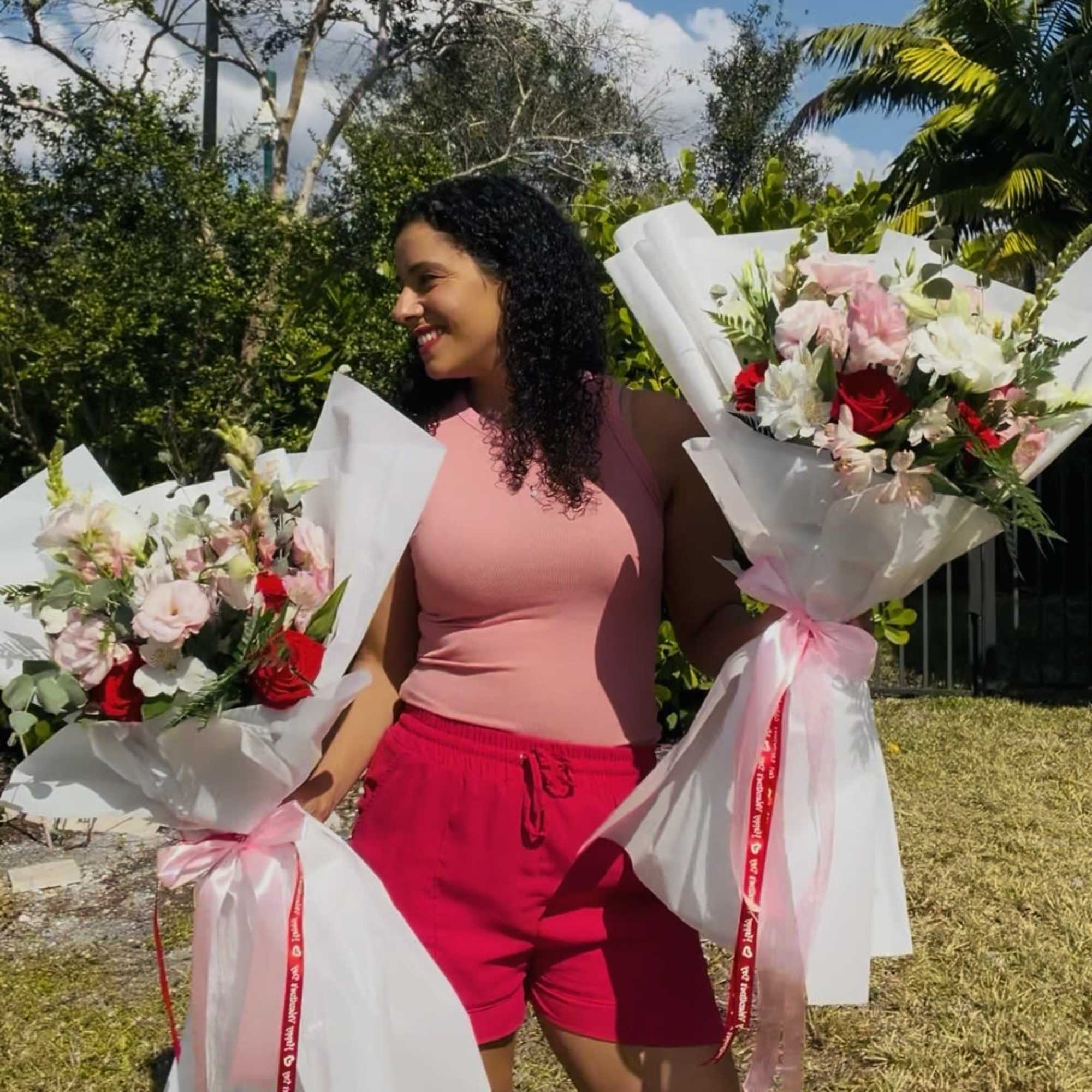 Woman holding two wrapped bouquets of pink, white, and red flowers outdoors