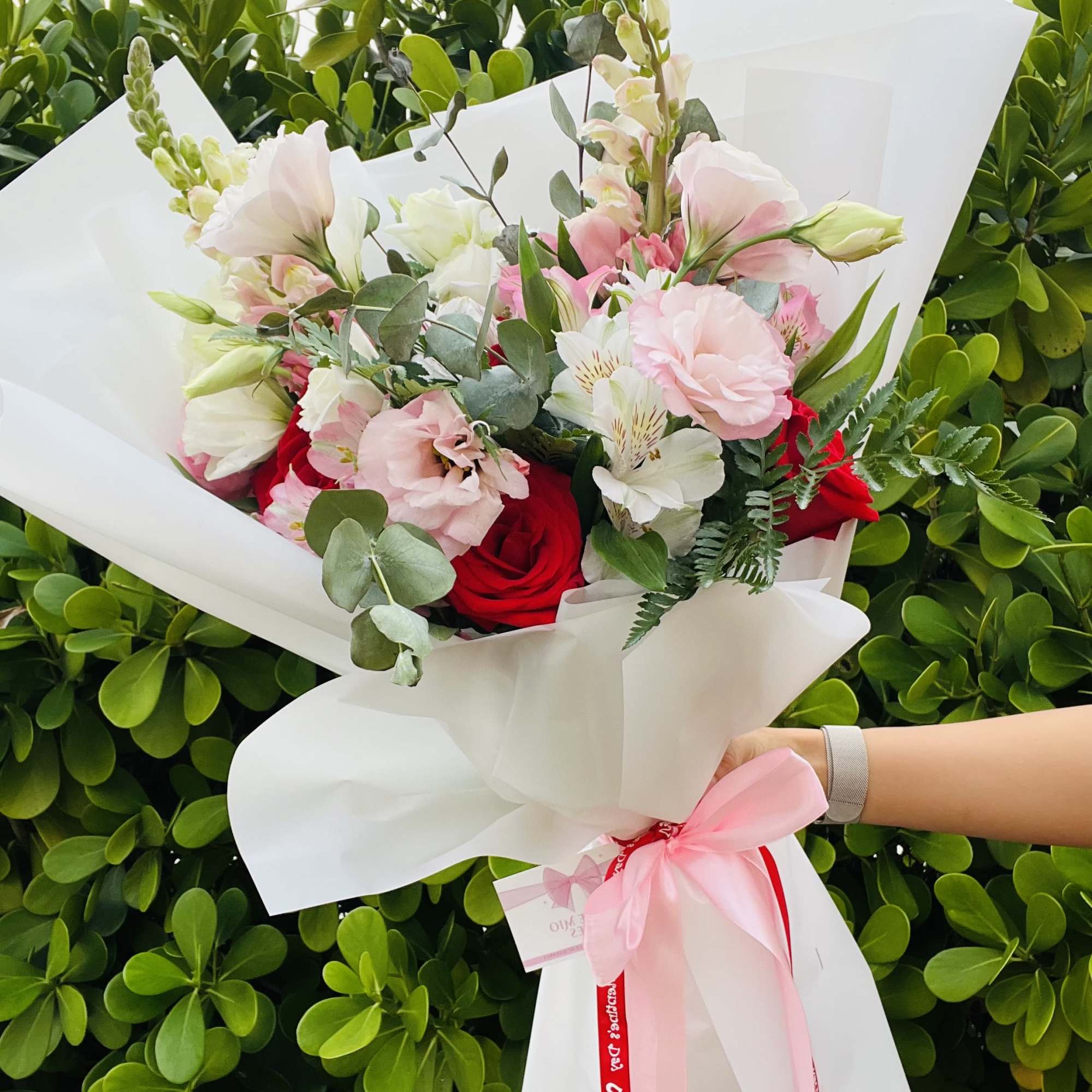 Handheld bouquet of pink and red flowers wrapped in white paper