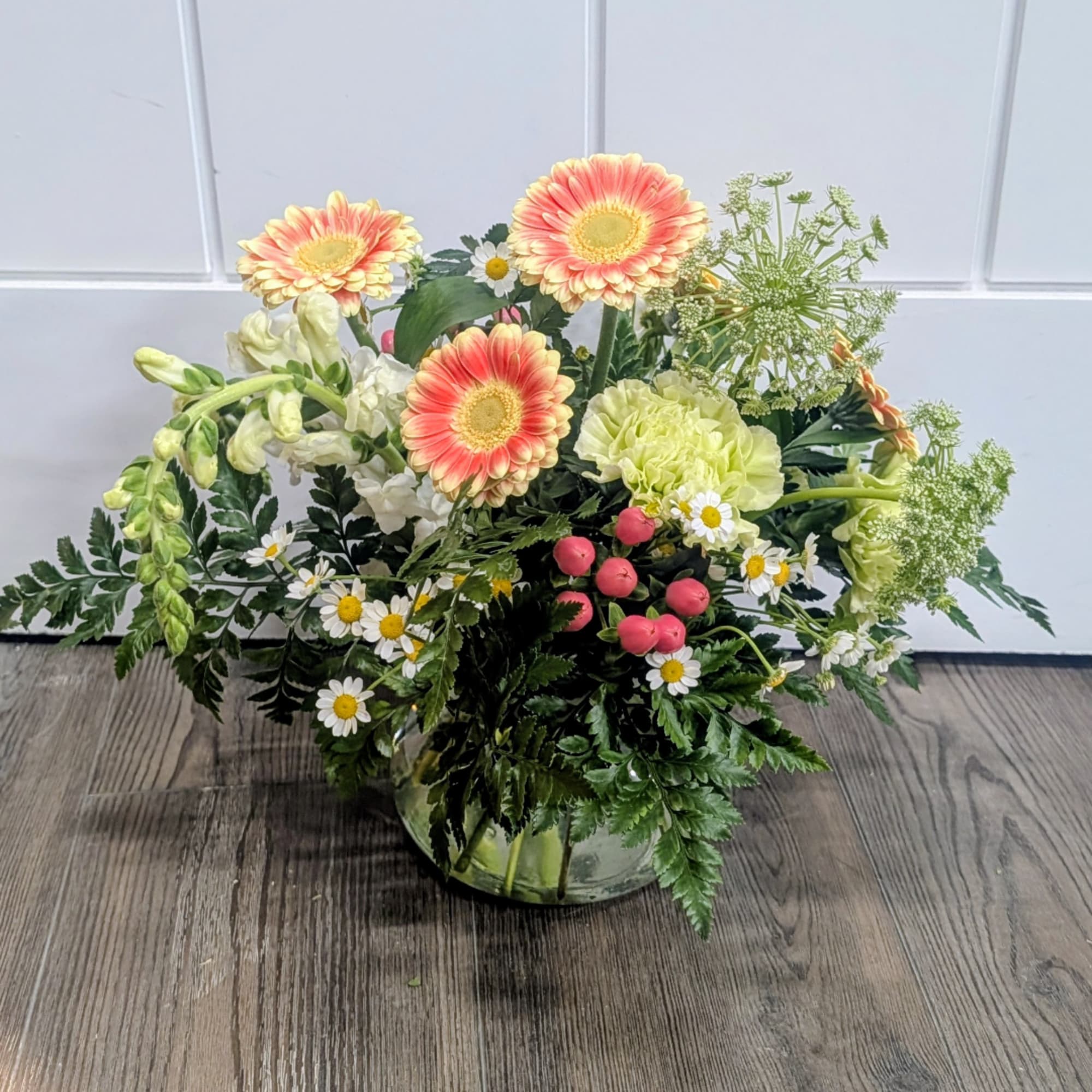 Mixed flower arrangement in a glass vase with peach gerberas and white blooms