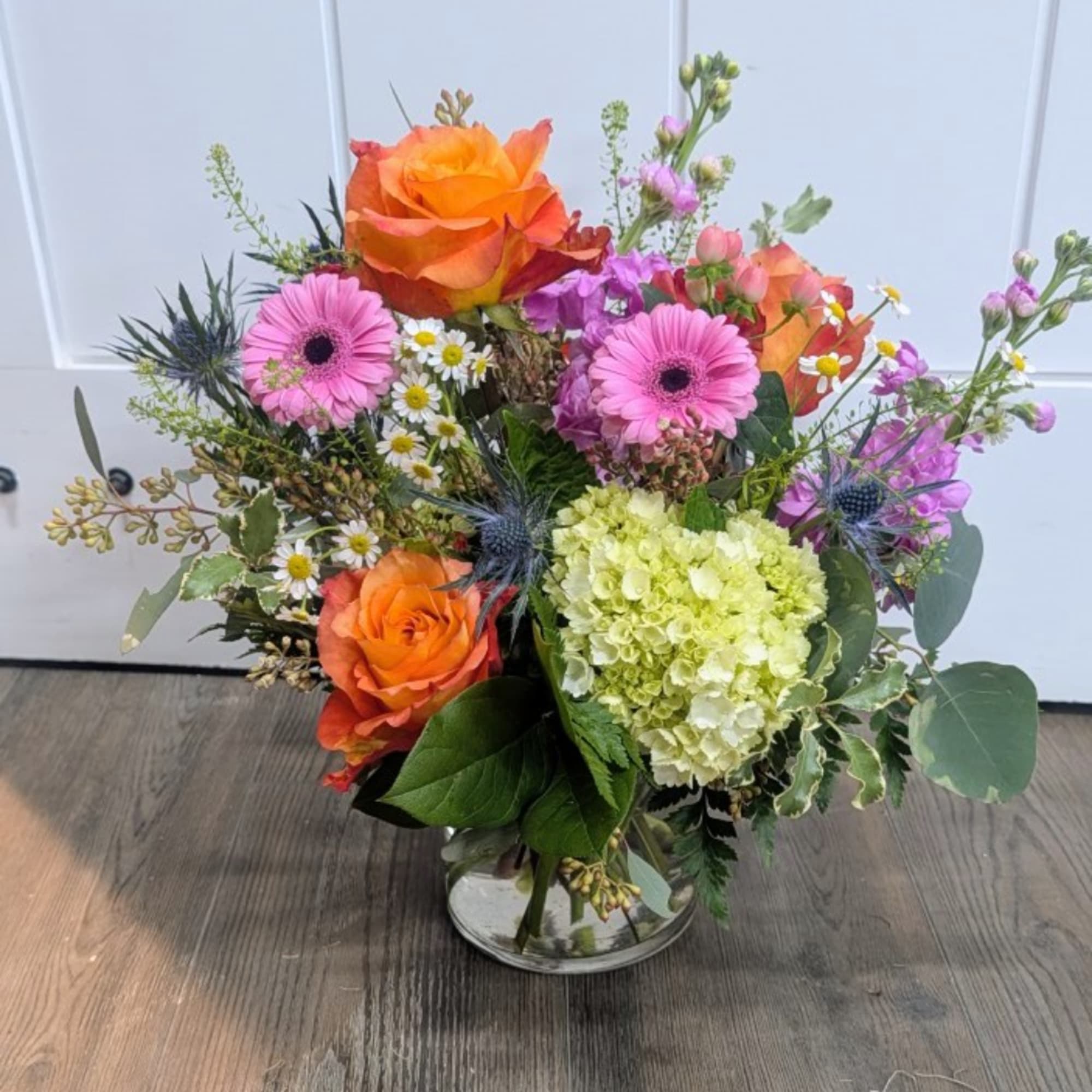 Mixed bouquet with orange roses, pink gerberas, and pale hydrangea in a glass vase