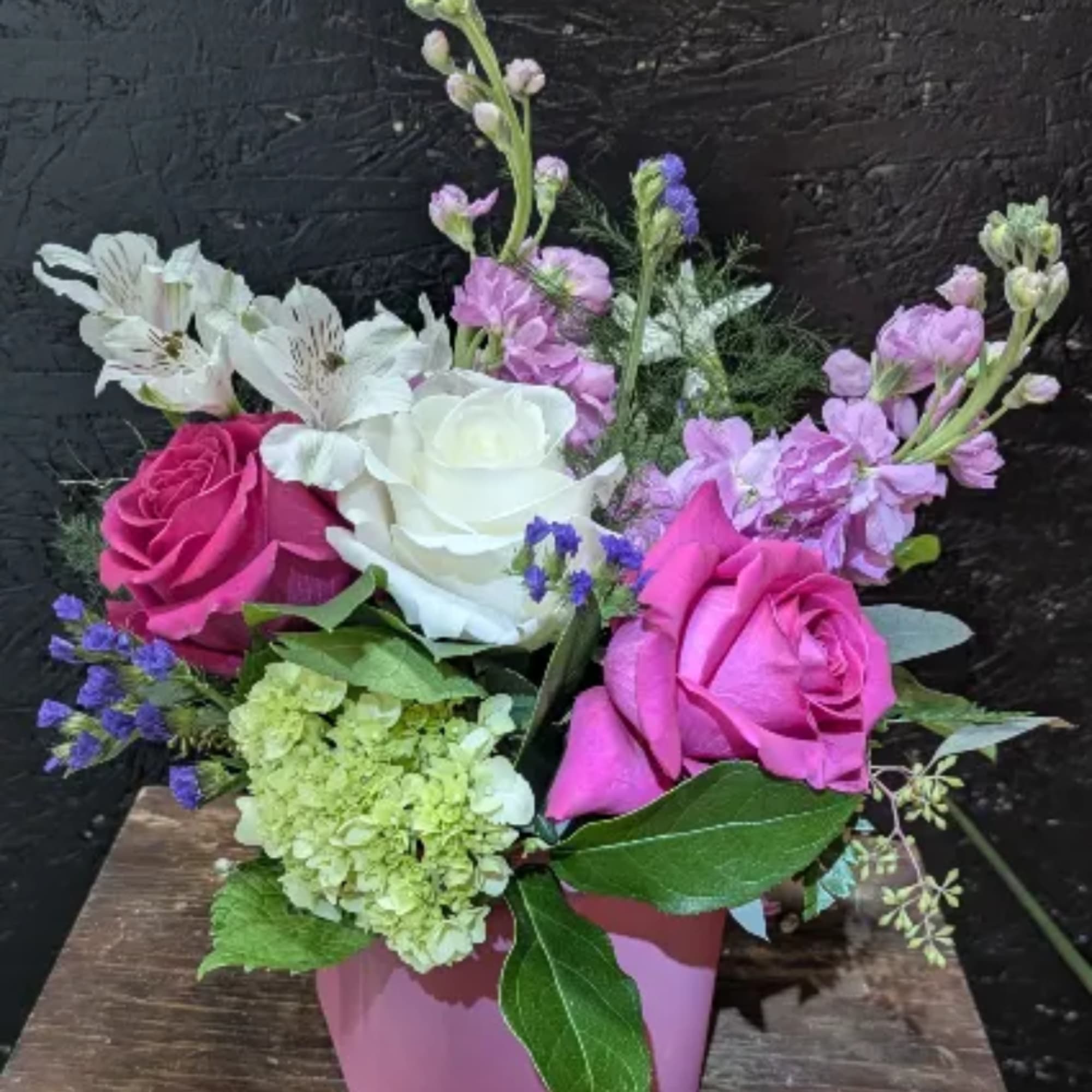 Pink and white roses with lavender flowers in a pink vase