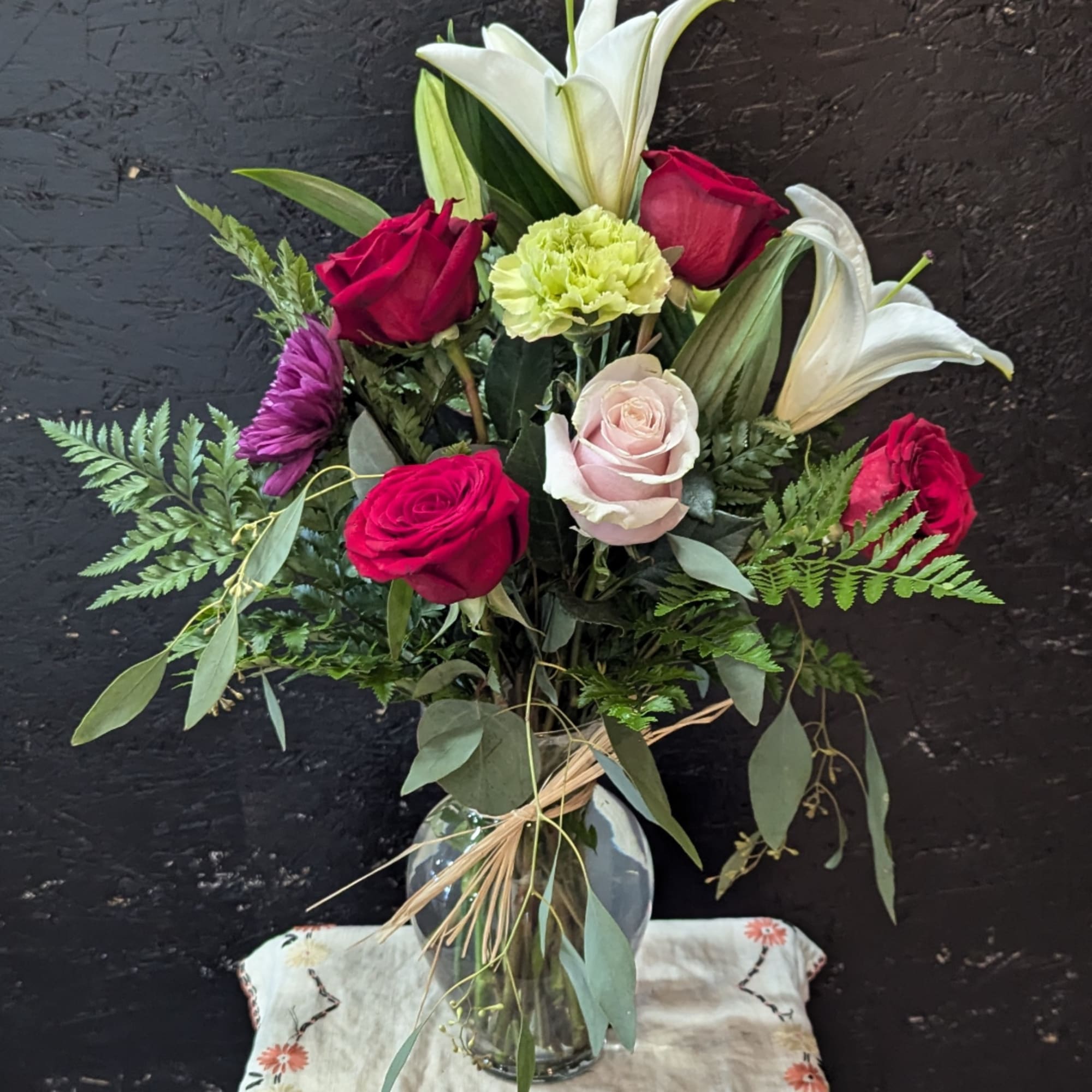 Mixed bouquet of roses, lilies, and a carnation in a glass vase
