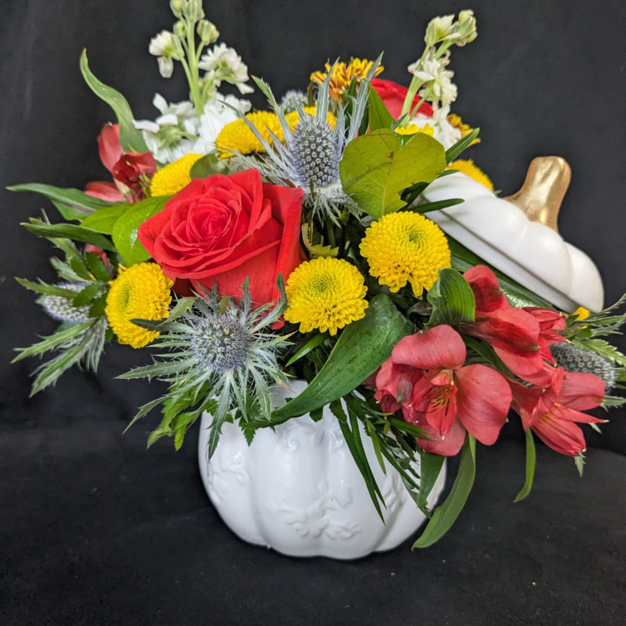 Mixed bouquet with red roses, yellow mums, and pink flowers in a white pumpkin vase