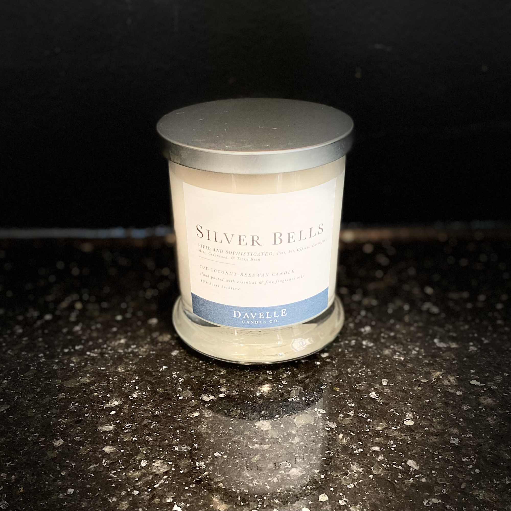 A silver-lidded candle in a glass jar on a dark countertop