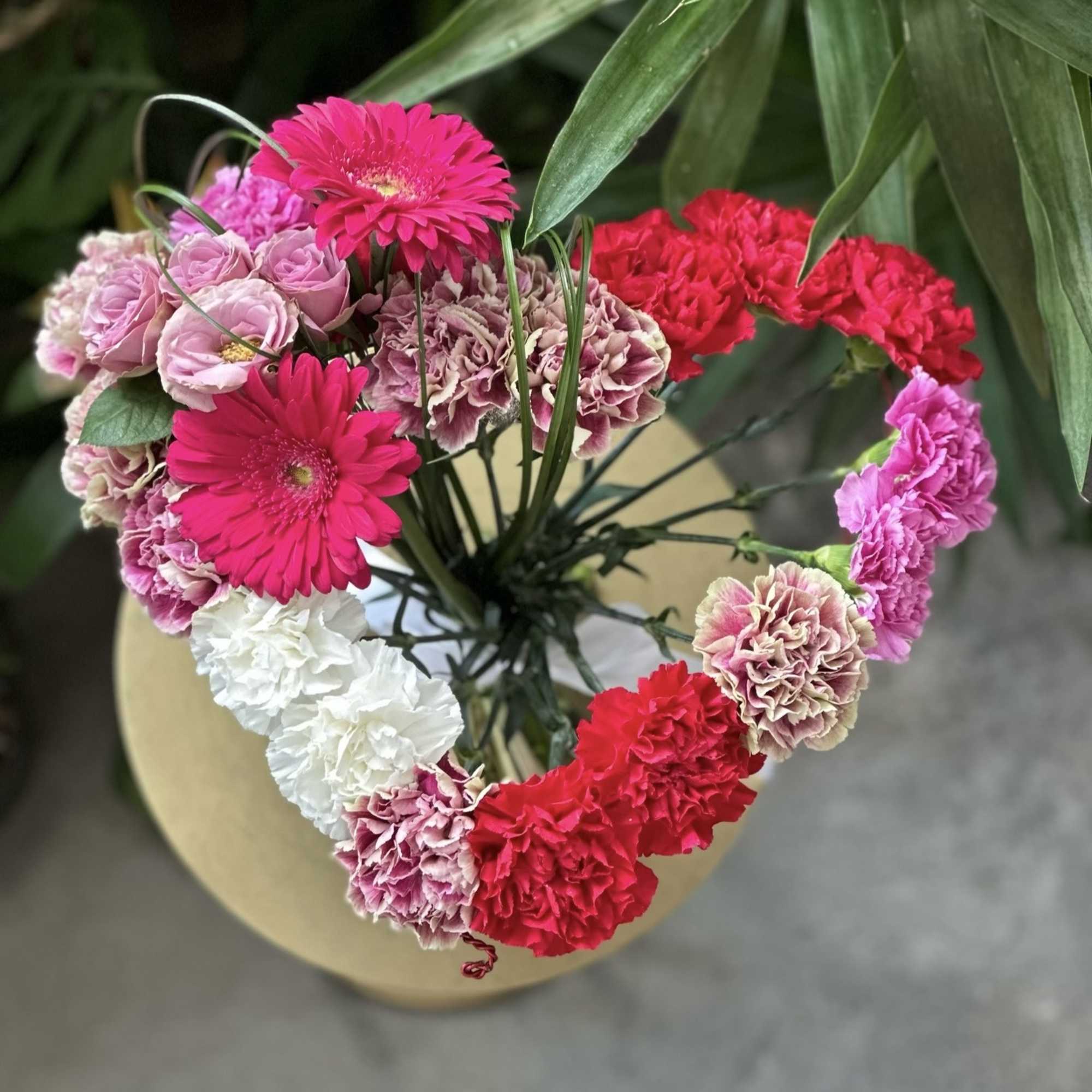 Heart-shaped bouquet of pink, red, and white carnations with gerbera daisies
