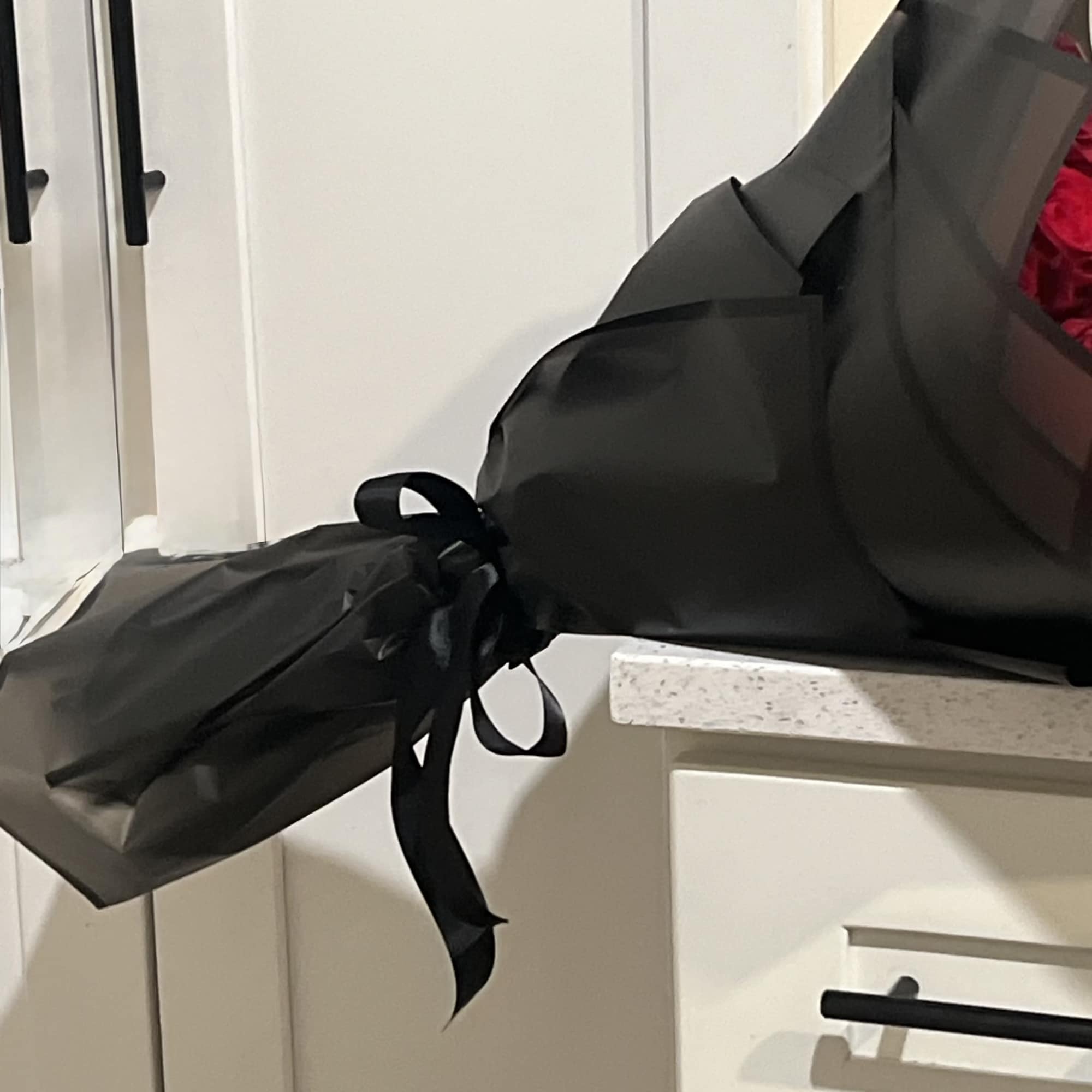 Black-wrapped bouquet with ribbon, partly showing red flowers