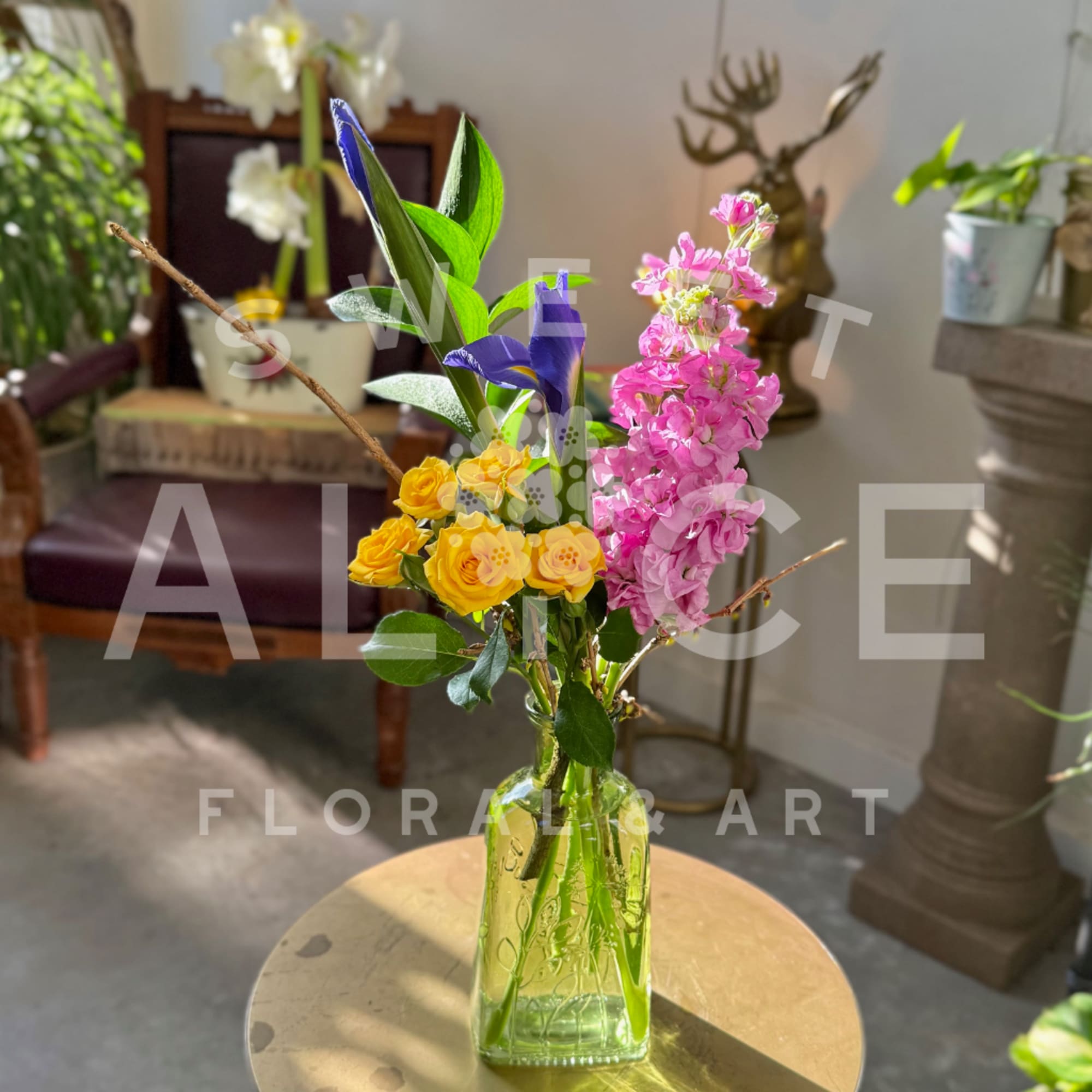 Yellow roses and pink blossoms in a clear glass vase with tall purple flowers.