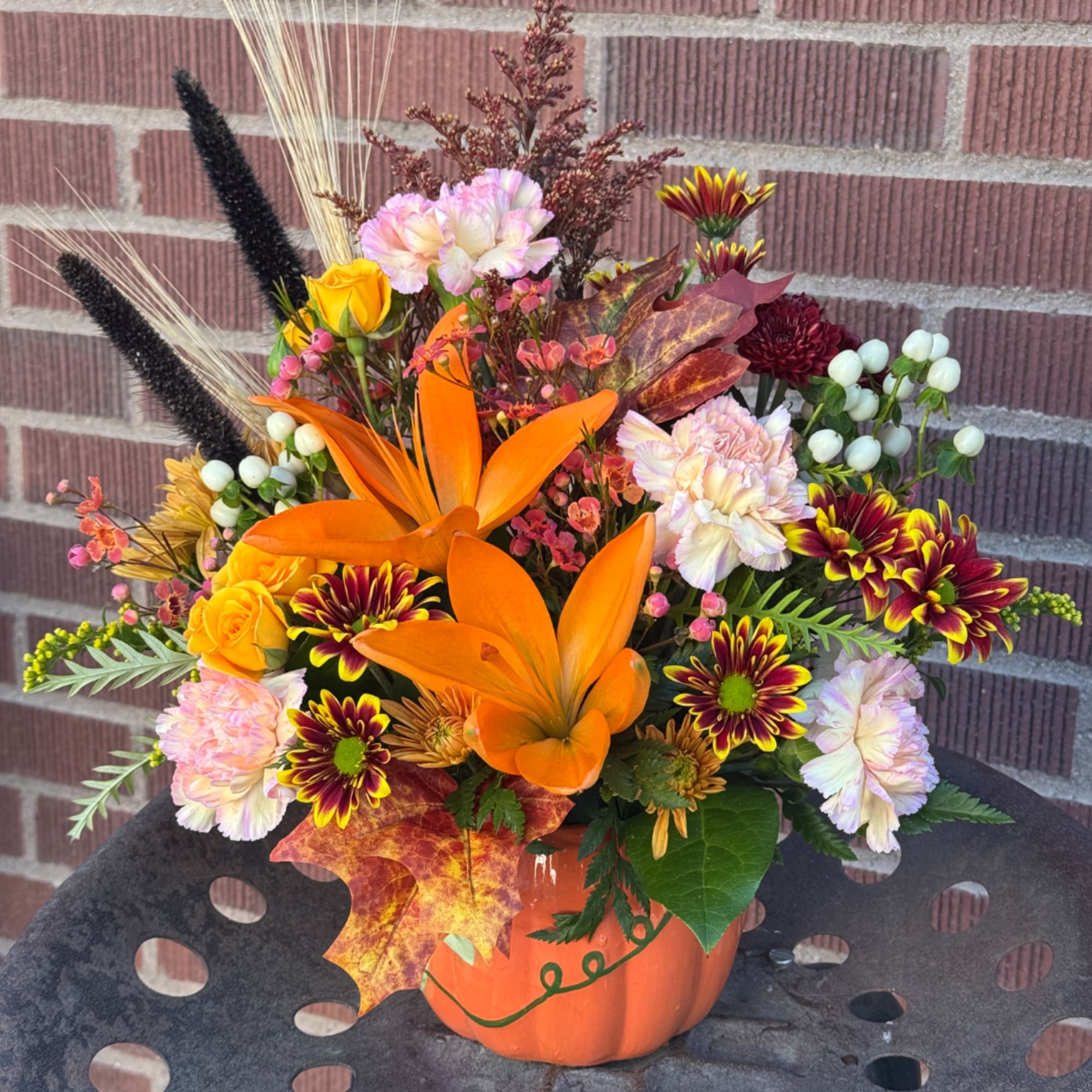 Autumn flower arrangement in an orange pumpkin container with lilies and mums