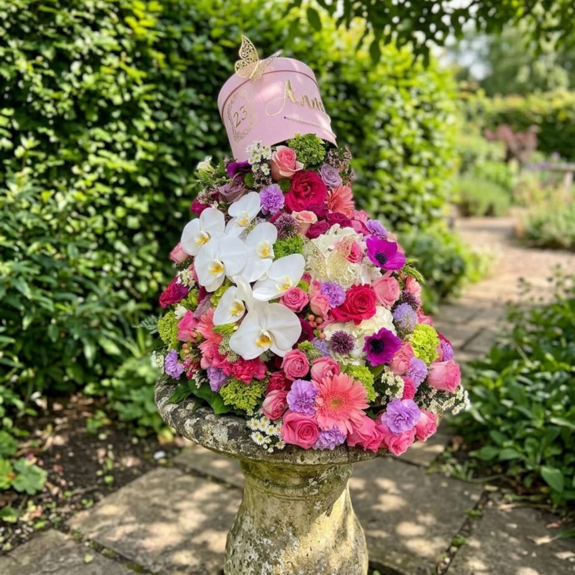 Pink floral arrangement in a hatbox on a stone pedestal