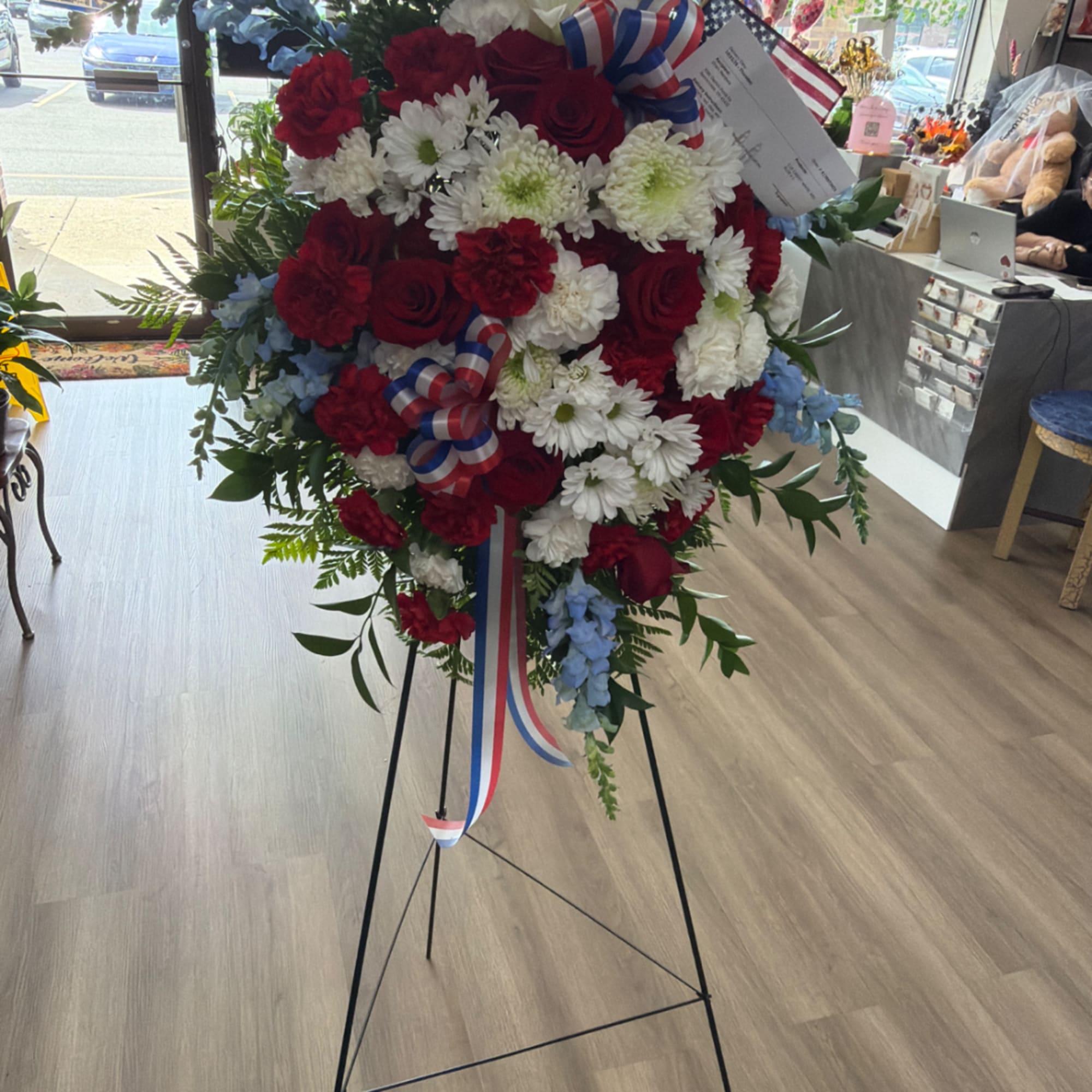 Red, white, and blue floral standing spray on an easel with ribbon streamers