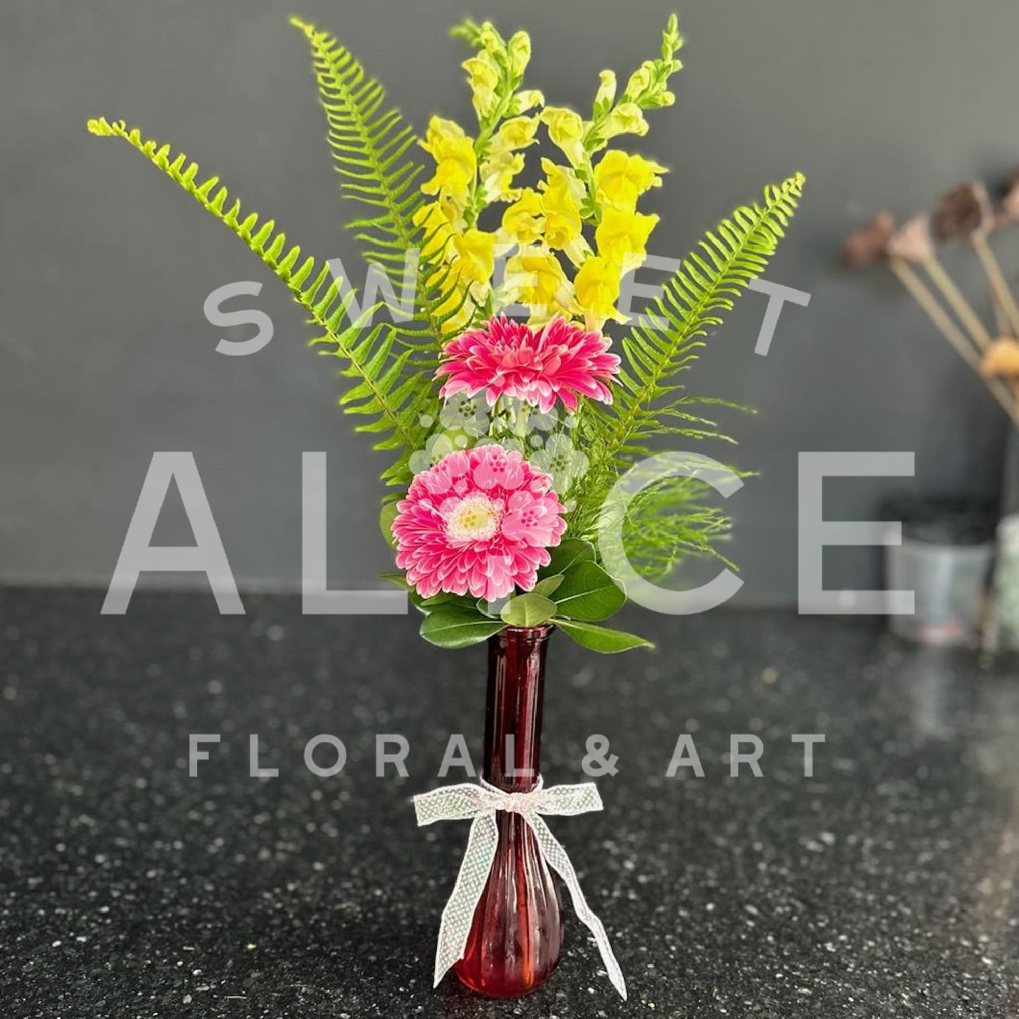 Pink flowers and yellow blooms in a red glass vase with a white ribbon