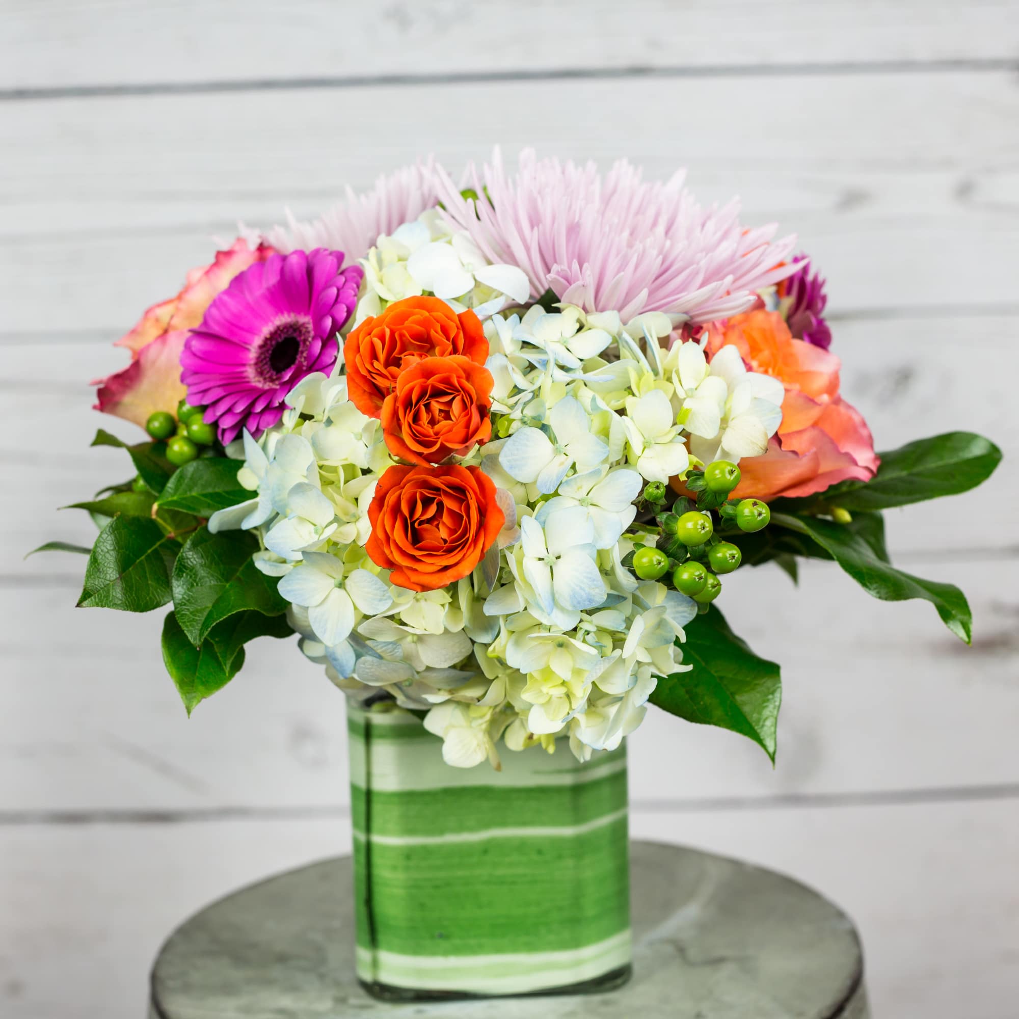 Colorful bouquet in a green glass vase with orange and pink flowers