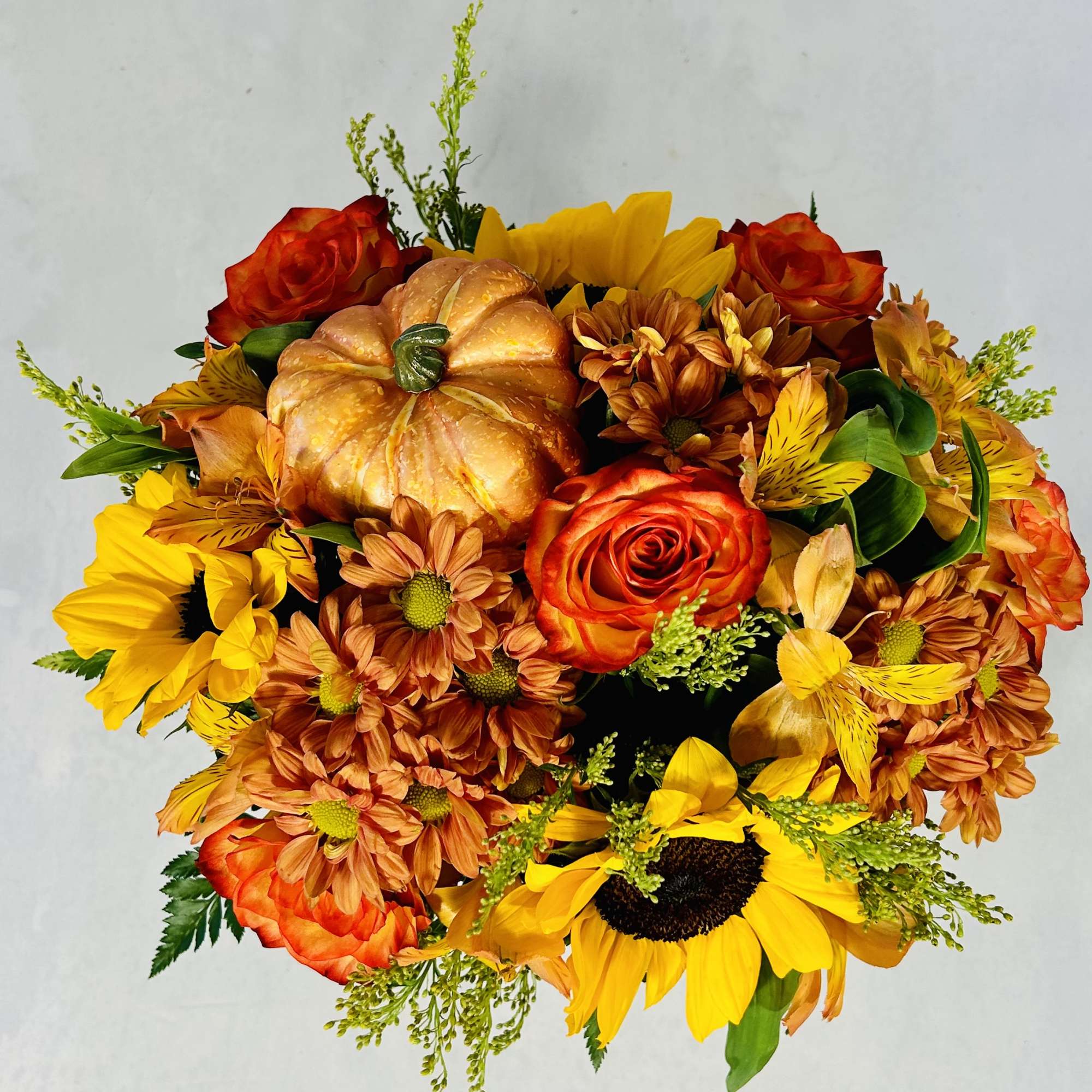 Bouquet of orange roses, sunflowers, and mums with a decorative pumpkin