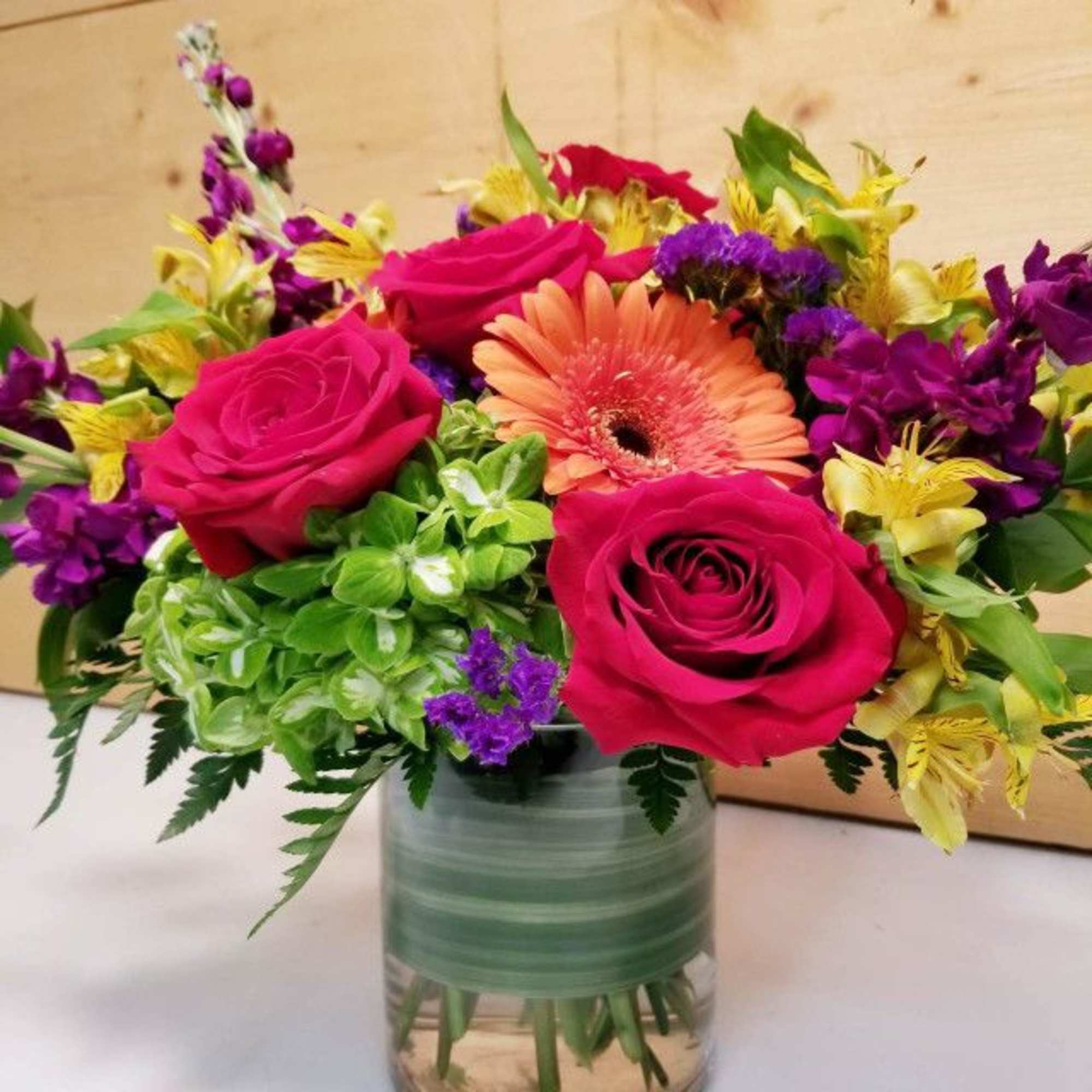 Bouquet of pink roses, a peach gerbera daisy, and purple flowers in a glass vase
