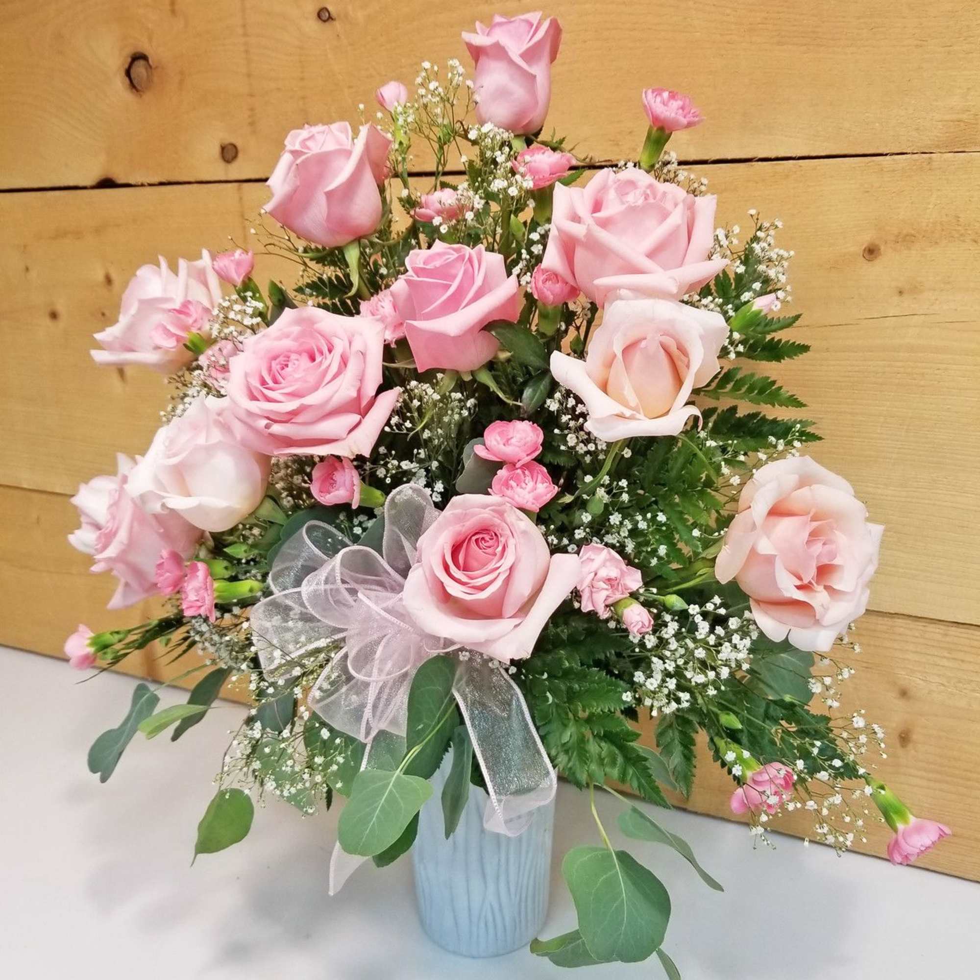Pink roses and baby's breath in a light blue vase with a sheer ribbon