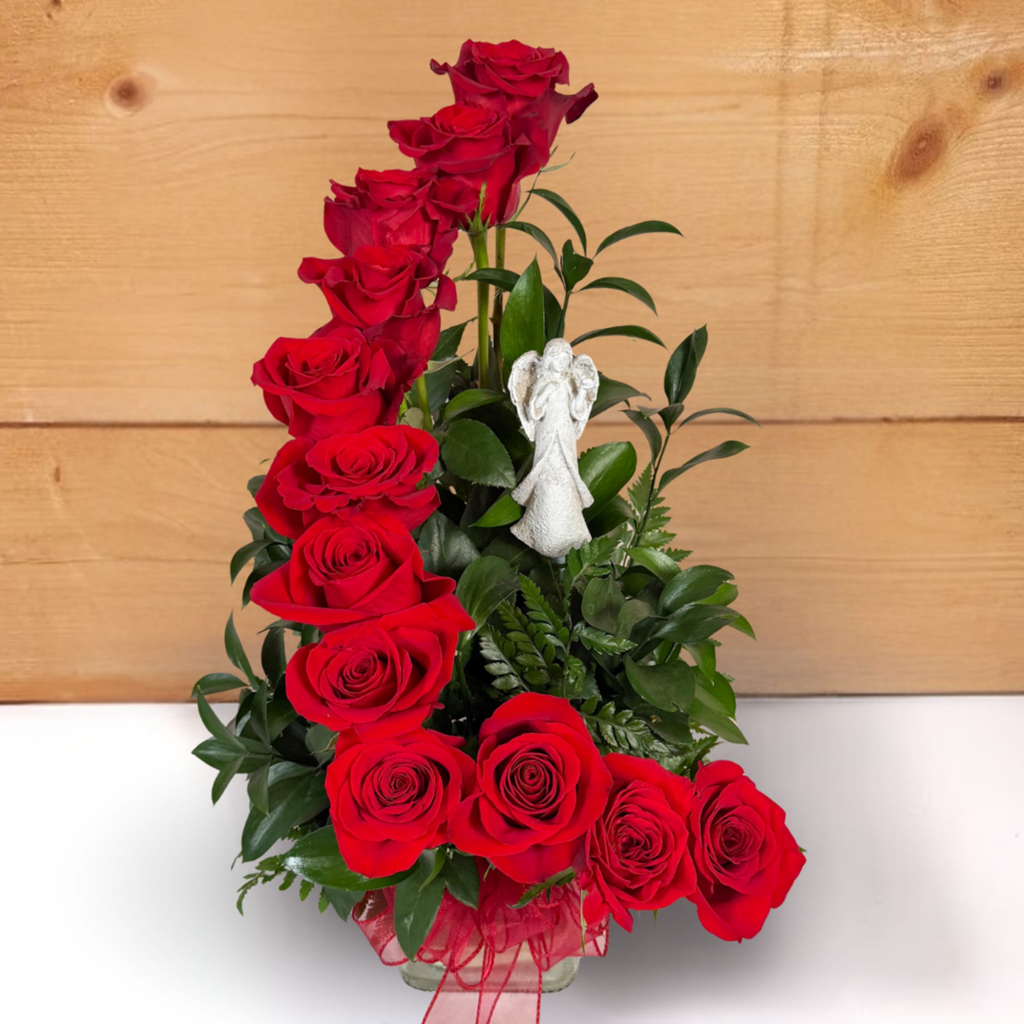 Red roses arranged in a tall vase with a small angel figurine