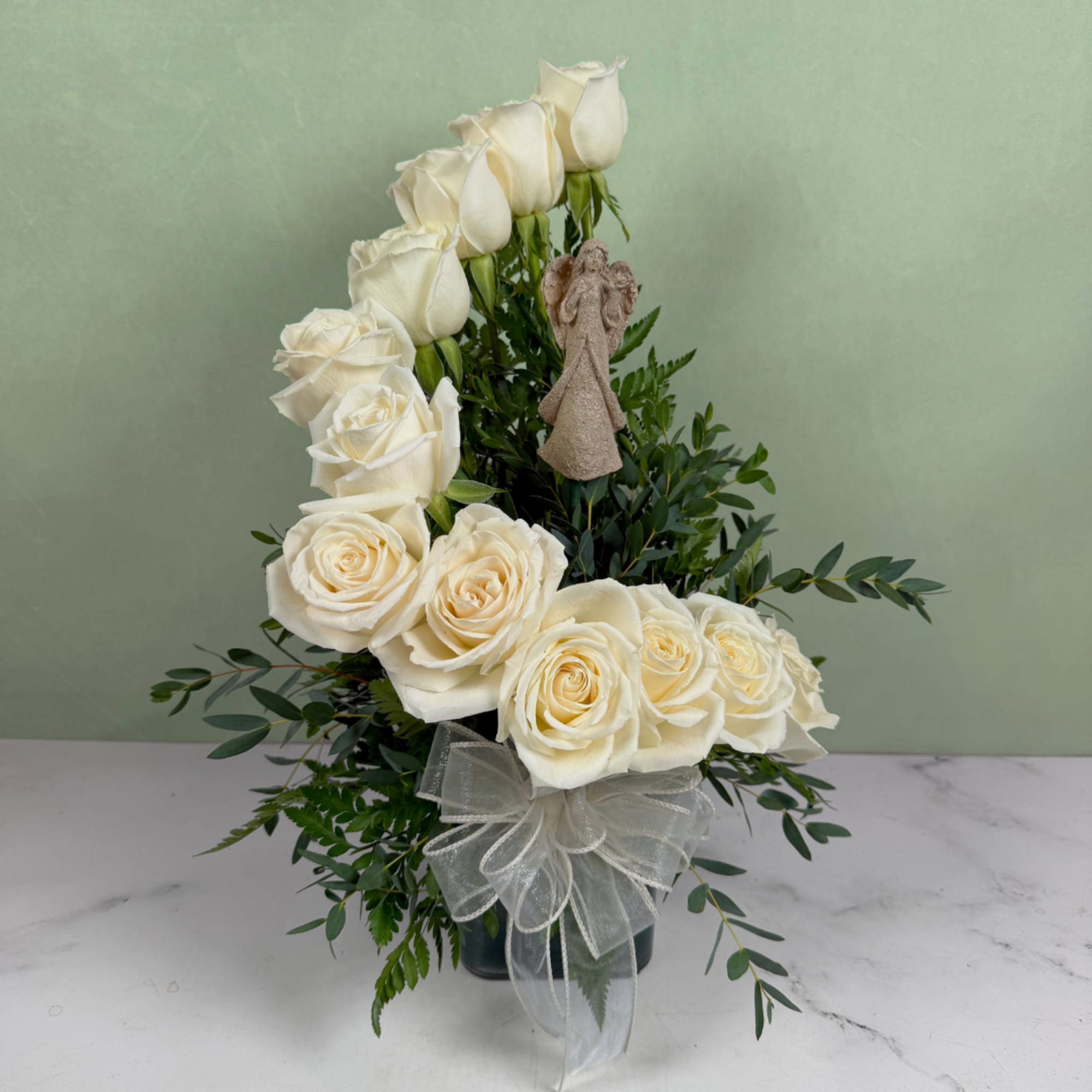 White roses arranged in a vase with greenery and a sheer bow
