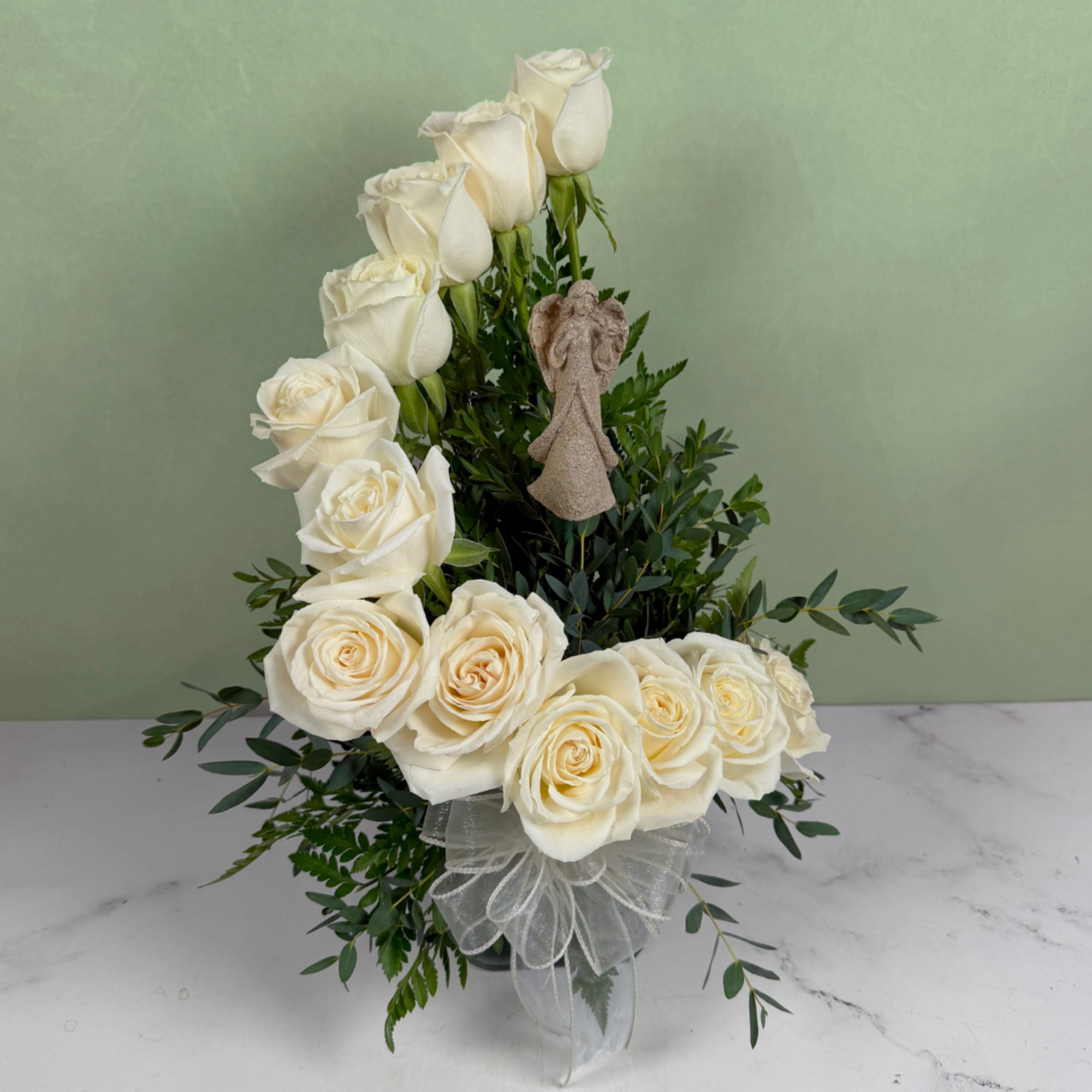 White roses arranged in a tall display with greenery and a sheer bow
