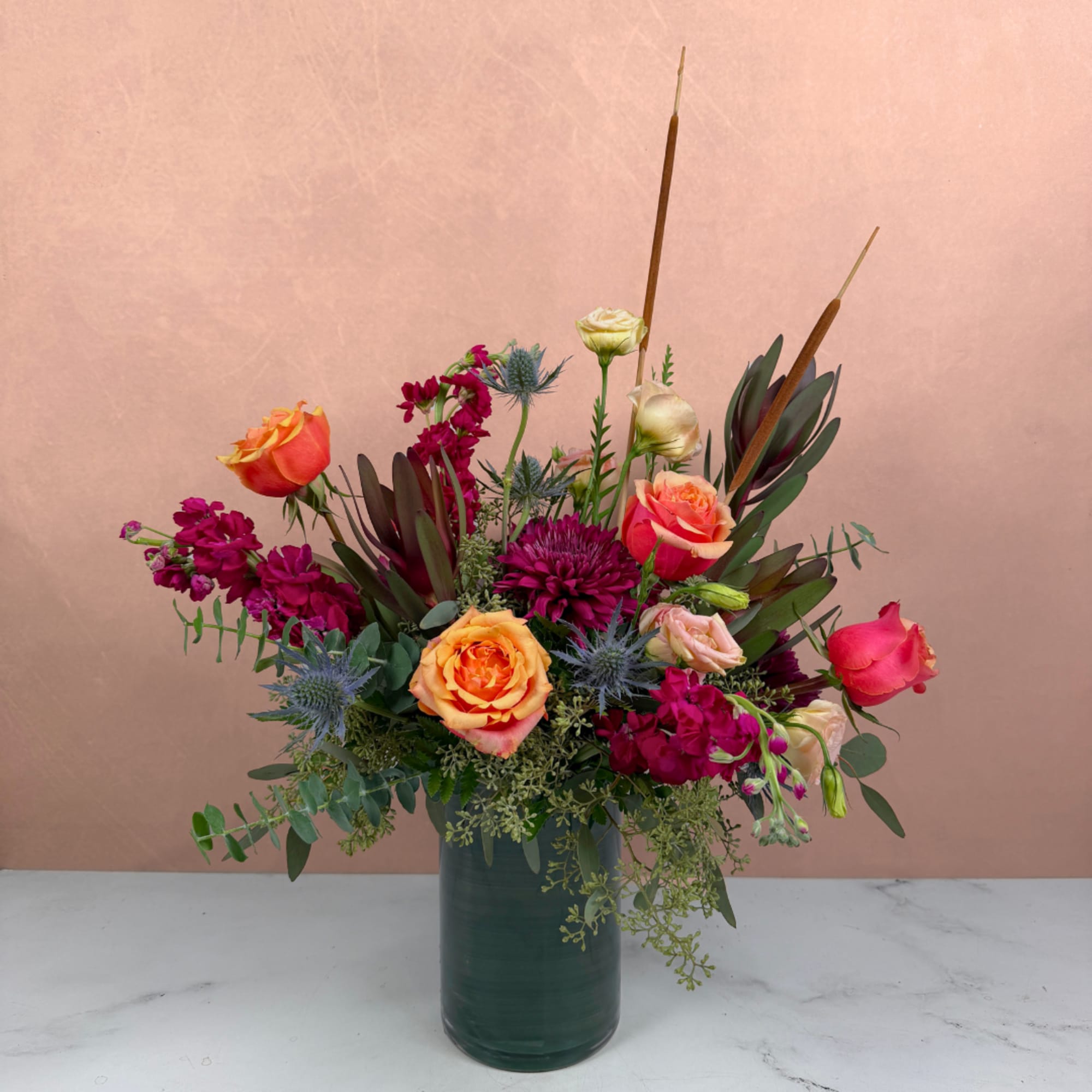 Mixed bouquet of roses and purple blooms in a dark green vase