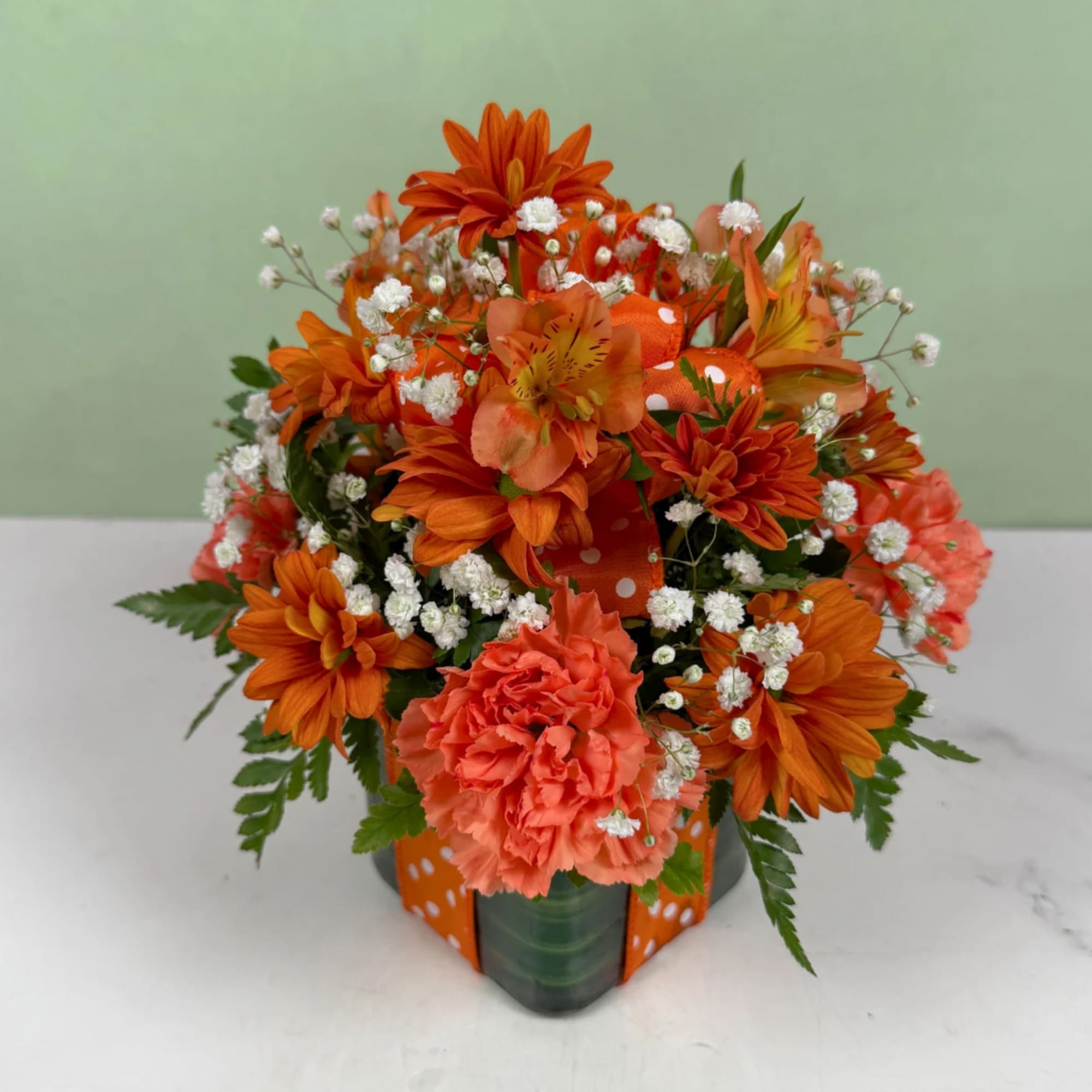 Orange mixed flower arrangement in a vase with white filler flowers