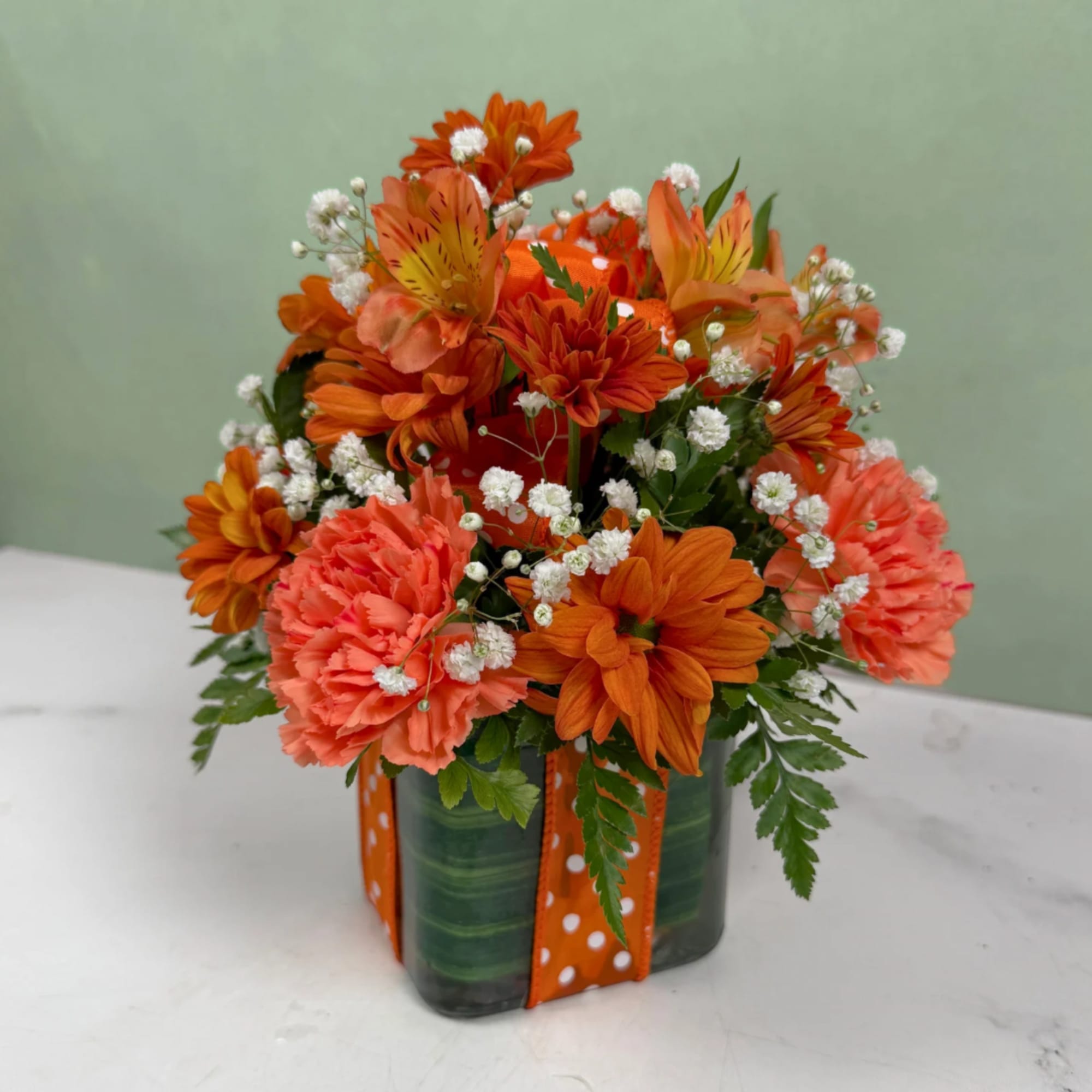 Orange and coral flower arrangement in a green vase with ribbon