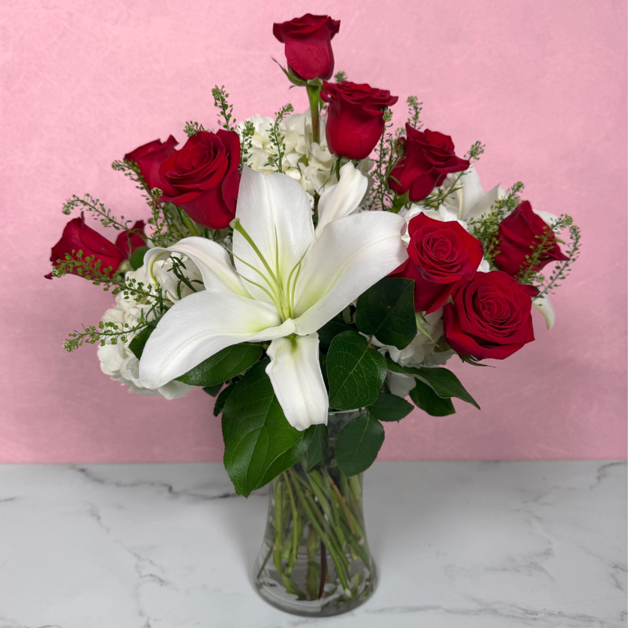 Red roses and a white lily in a clear glass vase.