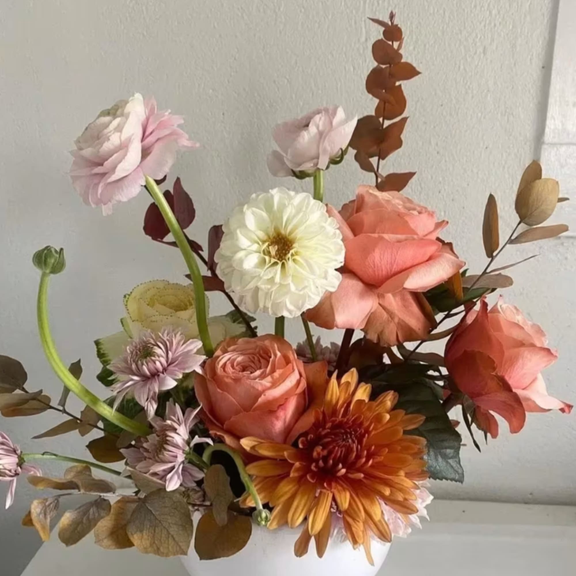 Mixed bouquet of pink roses, white dahlia, and orange chrysanthemum in a white vase