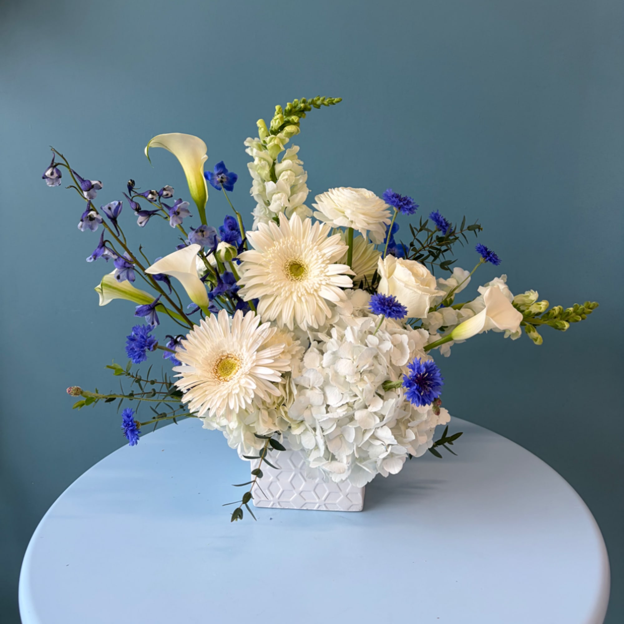 White and blue floral arrangement in a geometric white vase