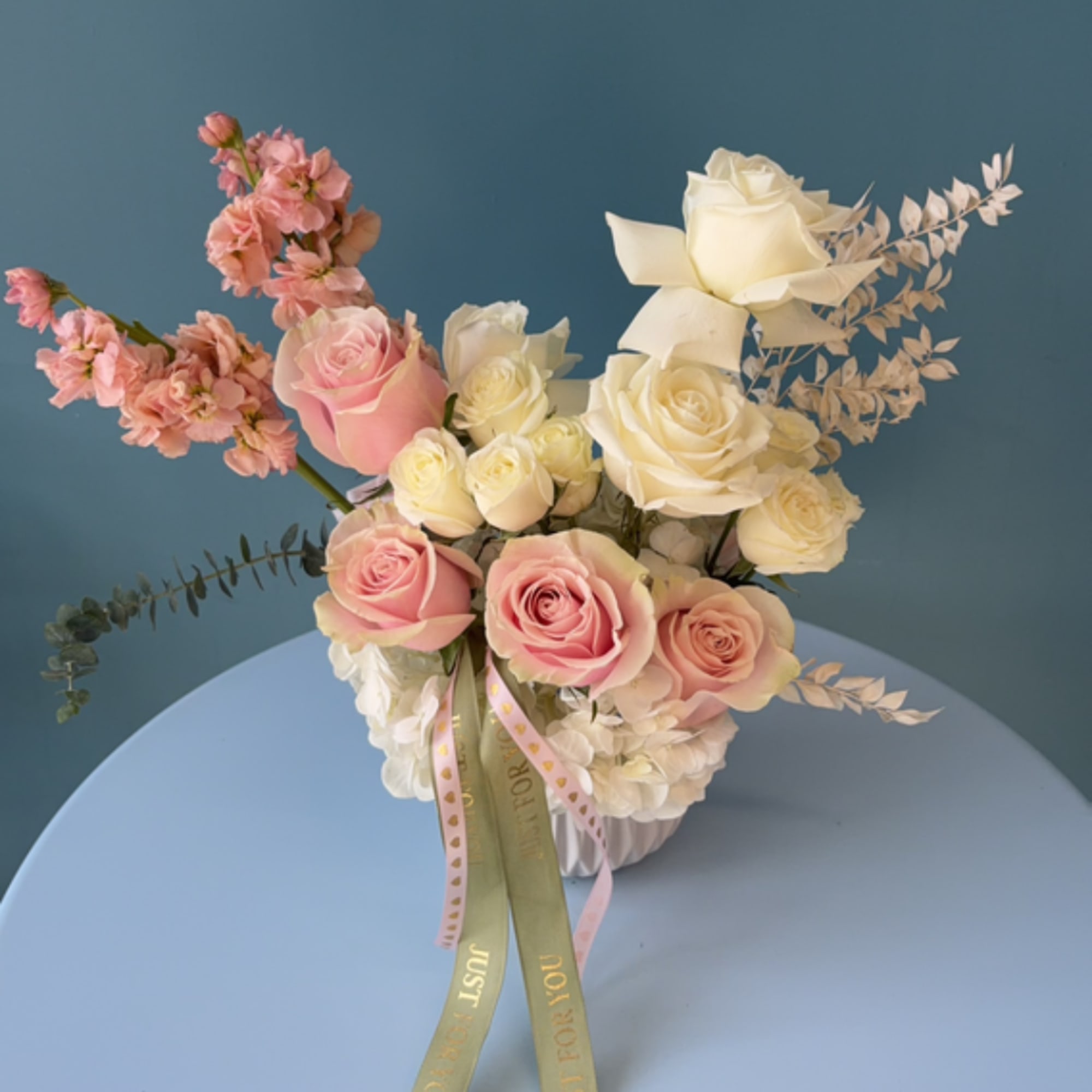 Pink and white roses arranged in a vase with ribbon accents