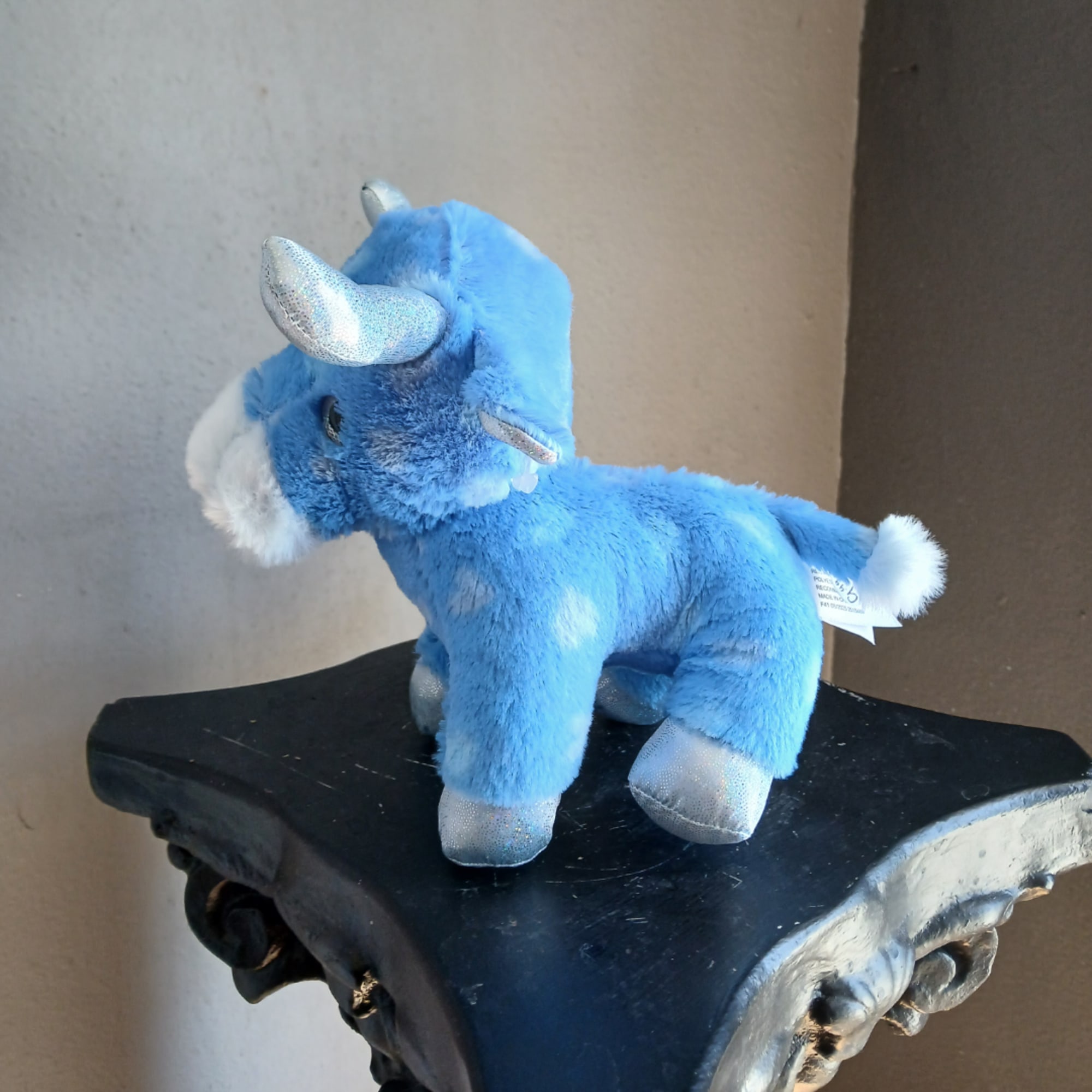 Blue plush unicorn toy with silver horns and hooves on a black pedestal