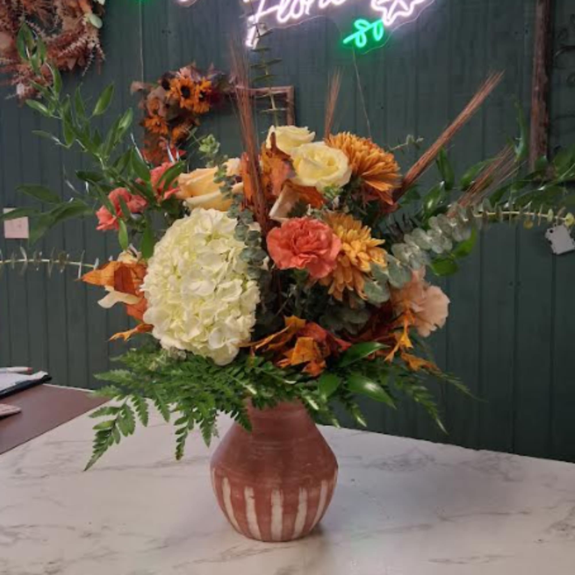 Autumn floral arrangement in a ceramic vase with roses, hydrangea, and mums