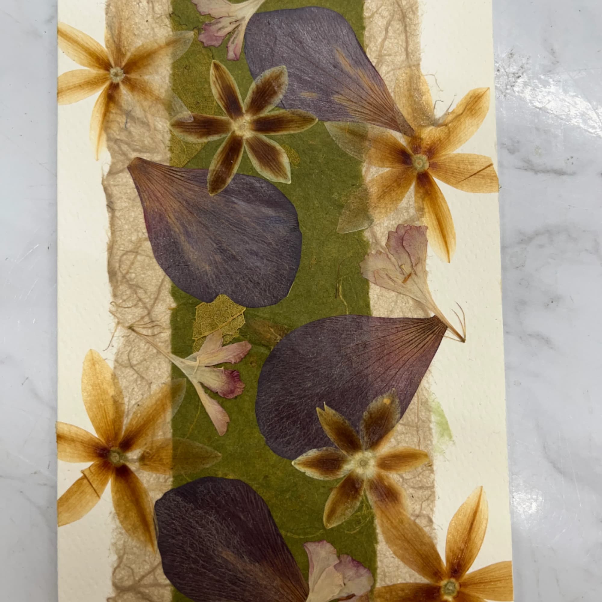 Pressed floral artwork with purple and gold petals on a cream background
