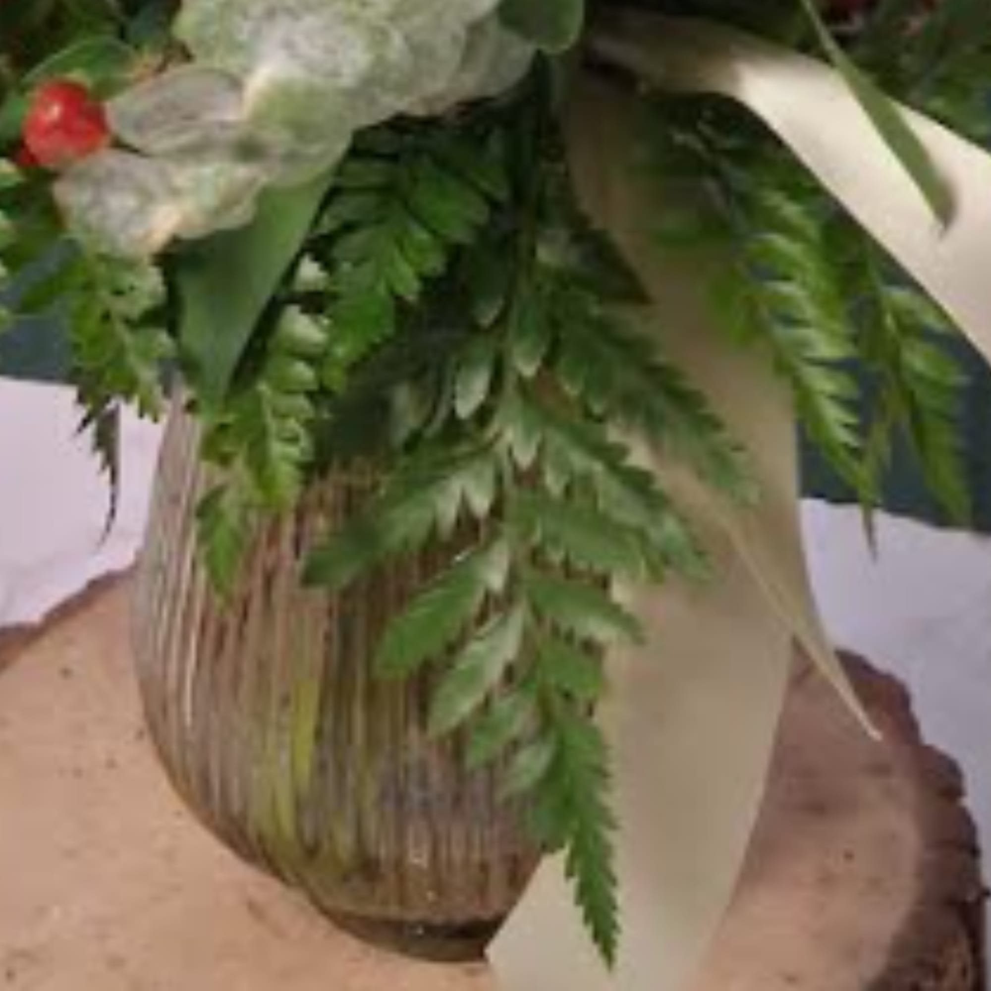 Green floral arrangement in a ribbed glass vase with white ribbon