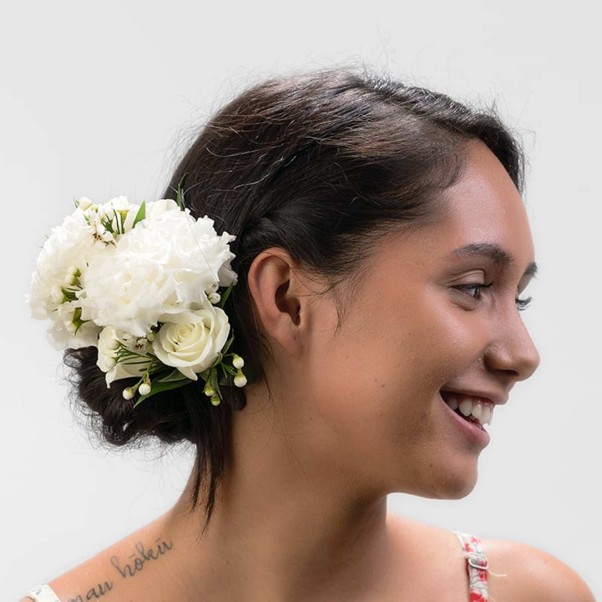 Woman with dark hair wearing a cluster of white roses and blooms as a low side hairpiece.