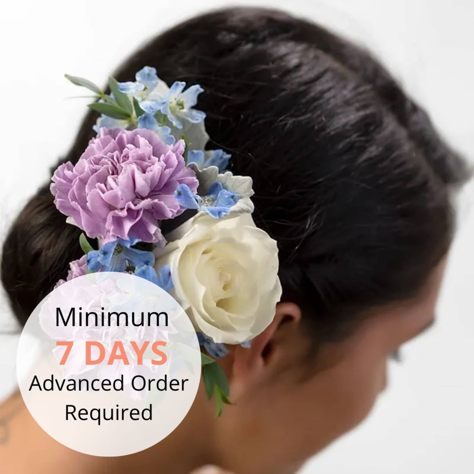 Floral hairpiece with purple carnation, white rose, and blue blooms worn in dark hair.