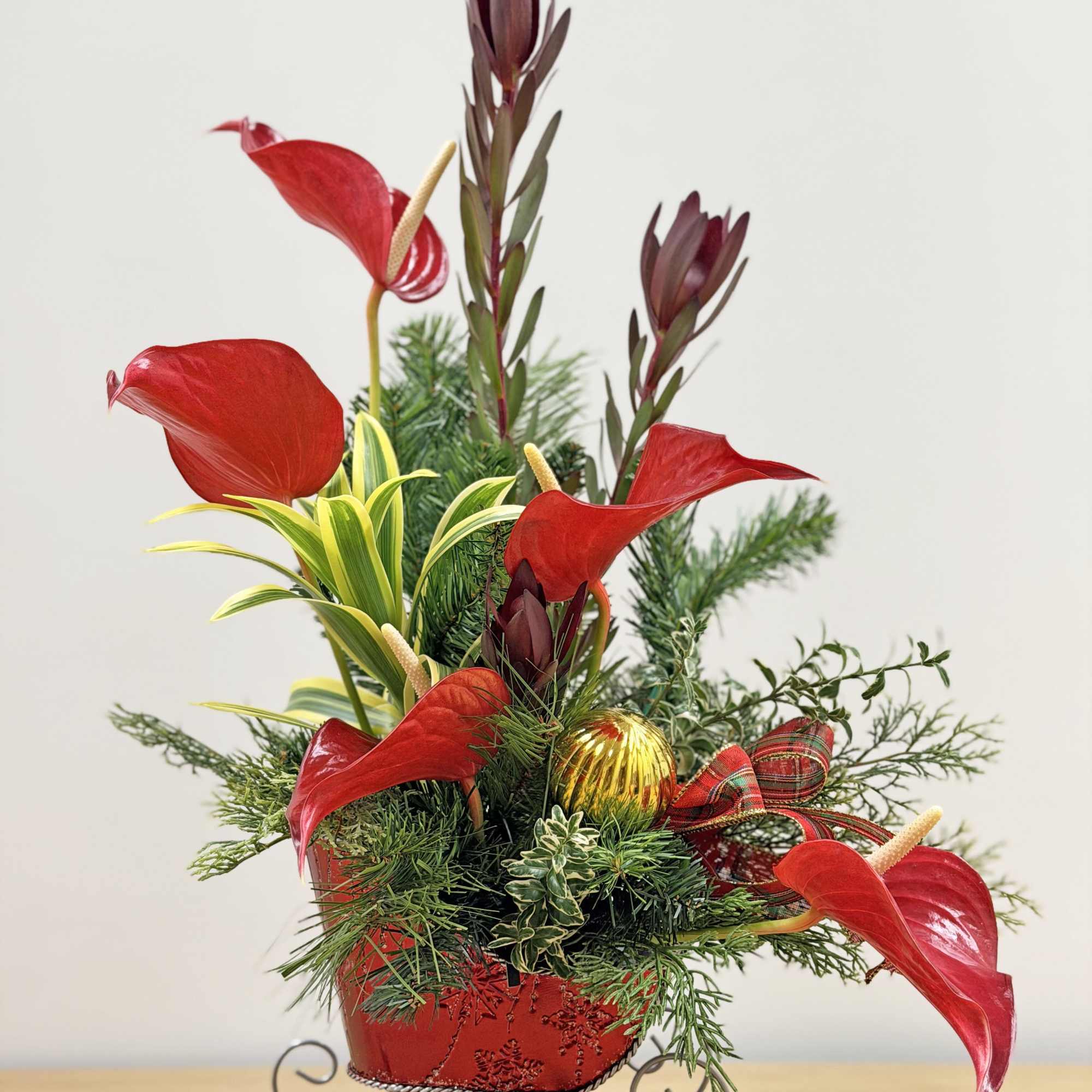 Red anthuriums arranged with evergreen branches in a red container.